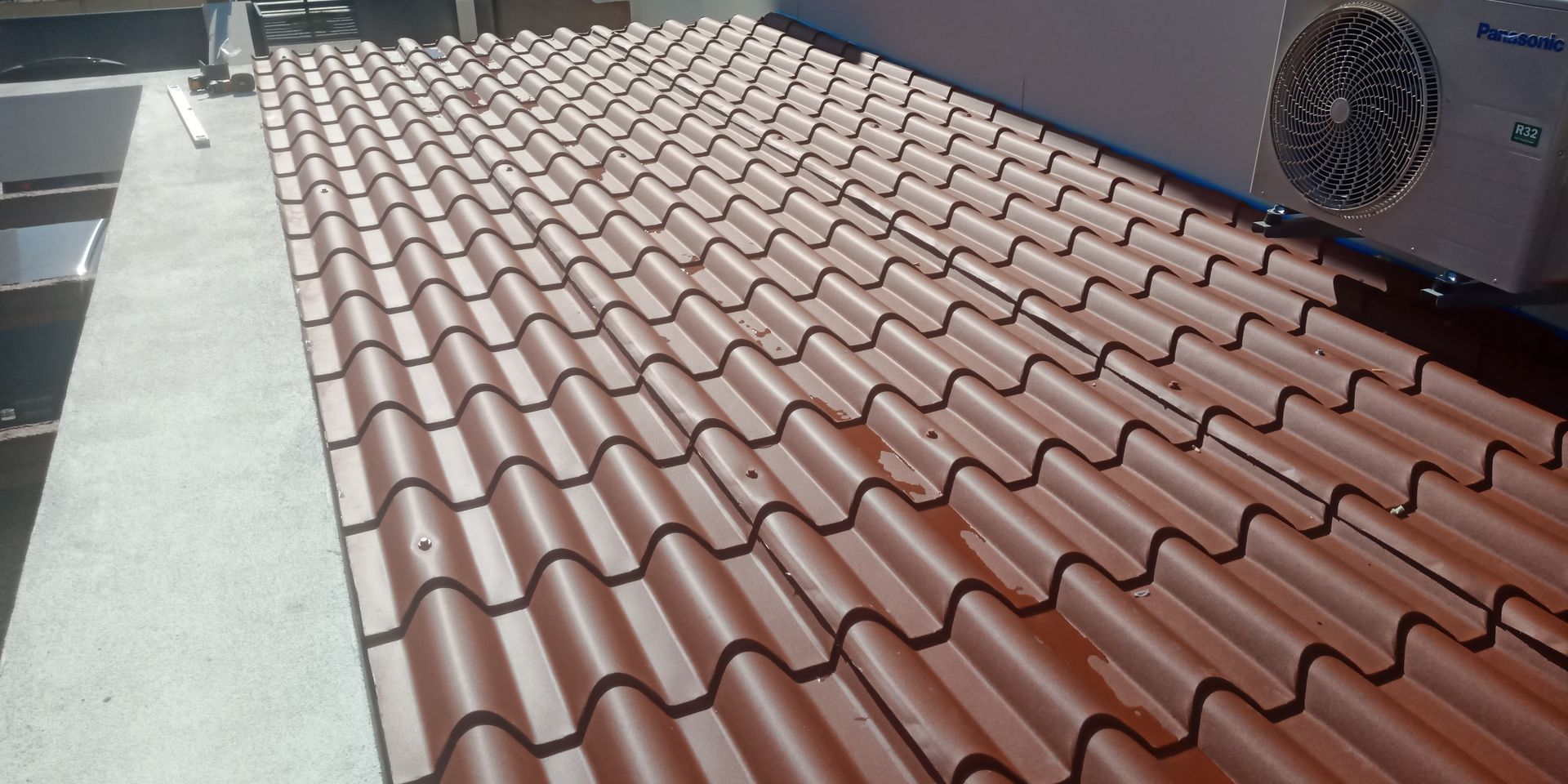 Telhado de metal ondulado vermelho. Unidade de ar condicionado no topo.