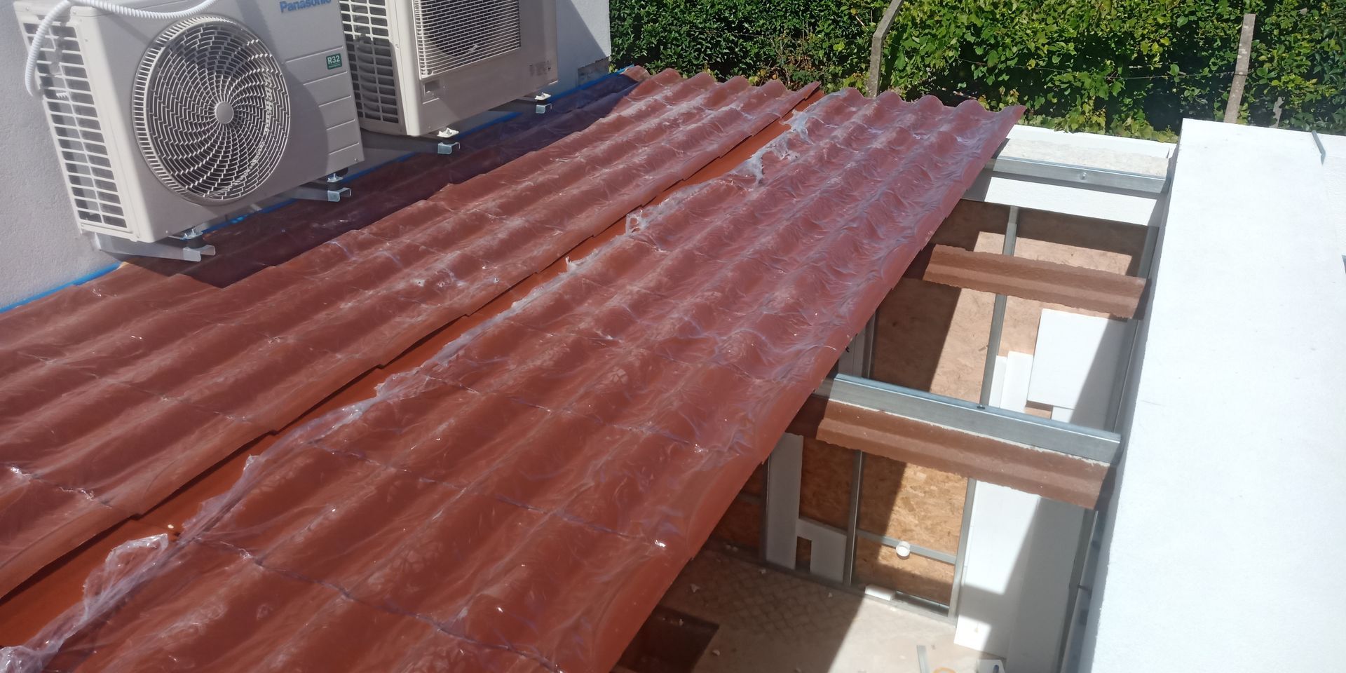 Chapas metálicas vermelhas onduladas sobre uma estrutura com unidades de ar condicionado e uma moldura de madeira.