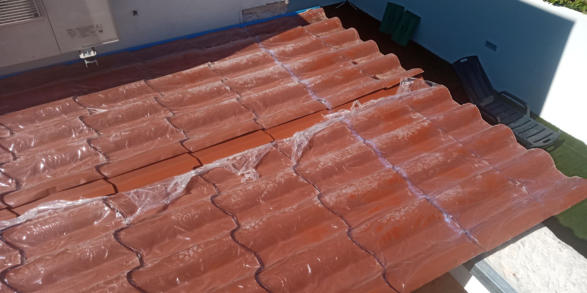 Telhado de telhas vermelhas parcialmente coberto com uma substância branca, provavelmente selante ou revestimento protetor, sob a luz solar.