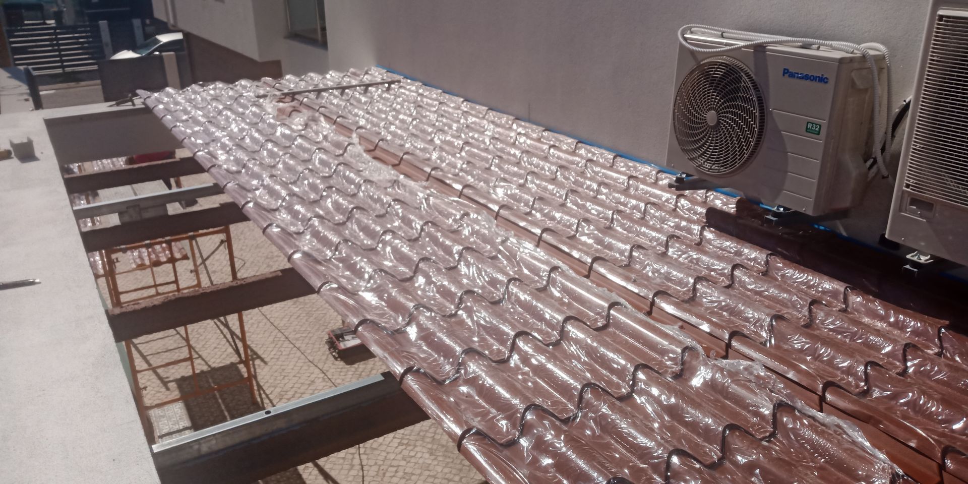 Vista de um telhado de telhas com unidades de ar condicionado e uma estrutura parcialmente exposta.