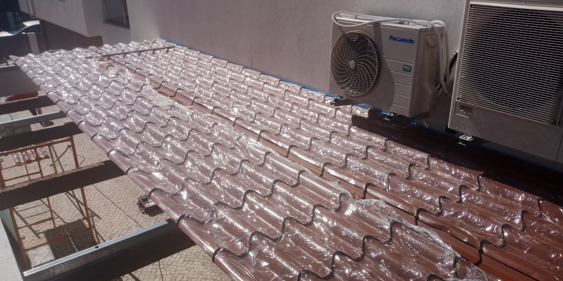 Cobertura com fileiras de objetos semelhantes a telhas, revestidos de plástico, e duas unidades de ar condicionado.