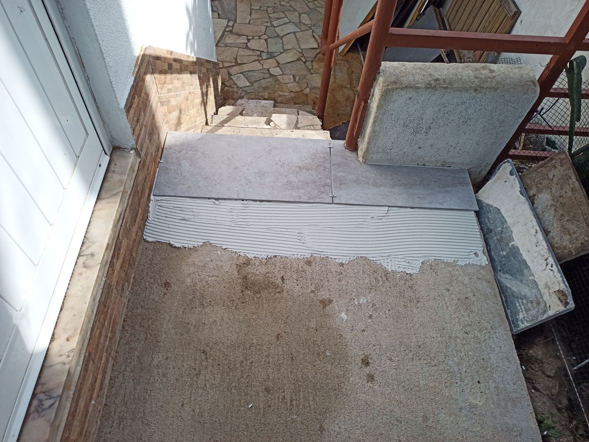 Degraus em construção; concreto com argamassa, ladrilhos de pedra cinza, estrutura metálica.