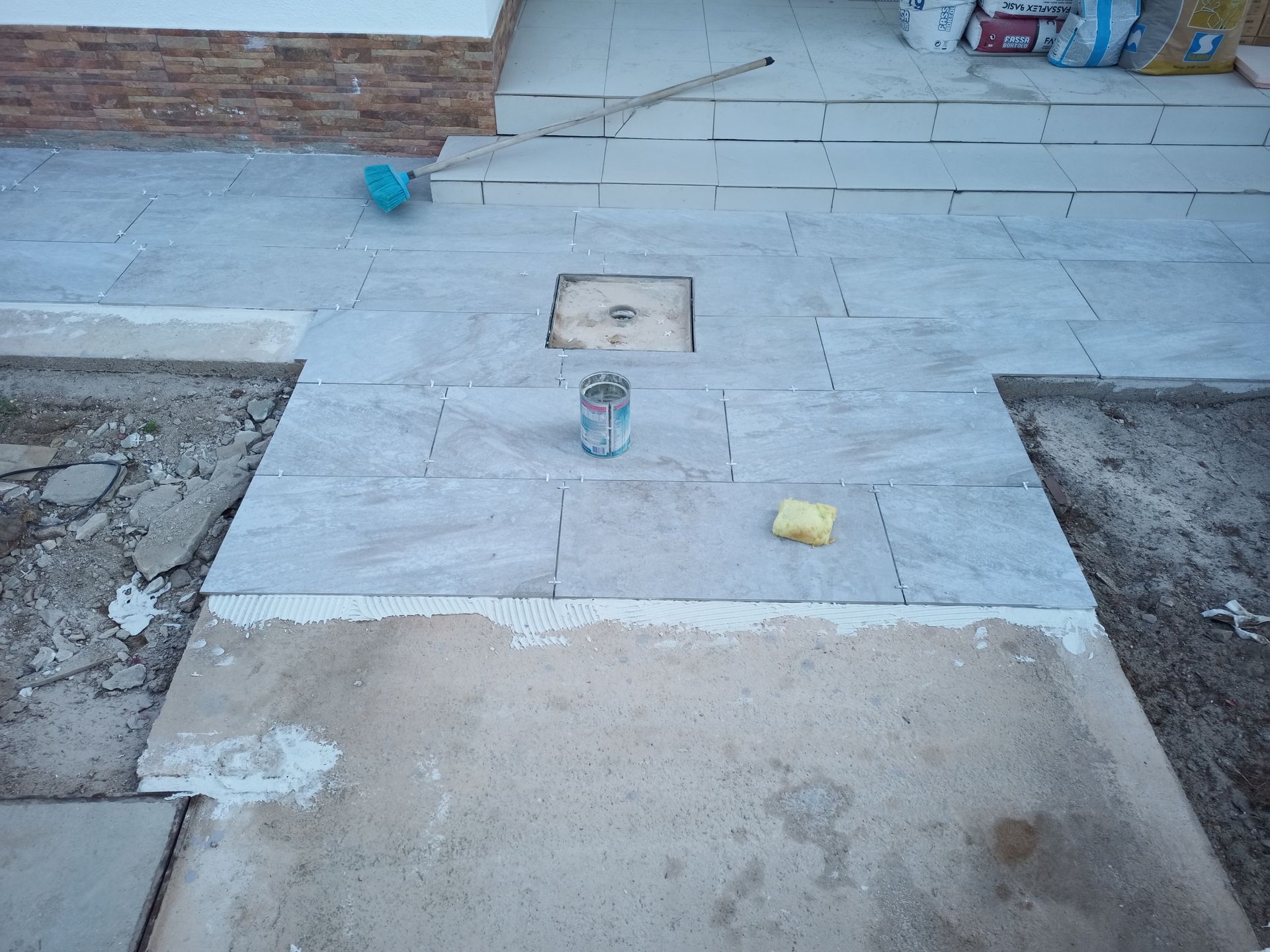 Caminho recém-azulejado em construção, utilizando cimento e ferramentas.