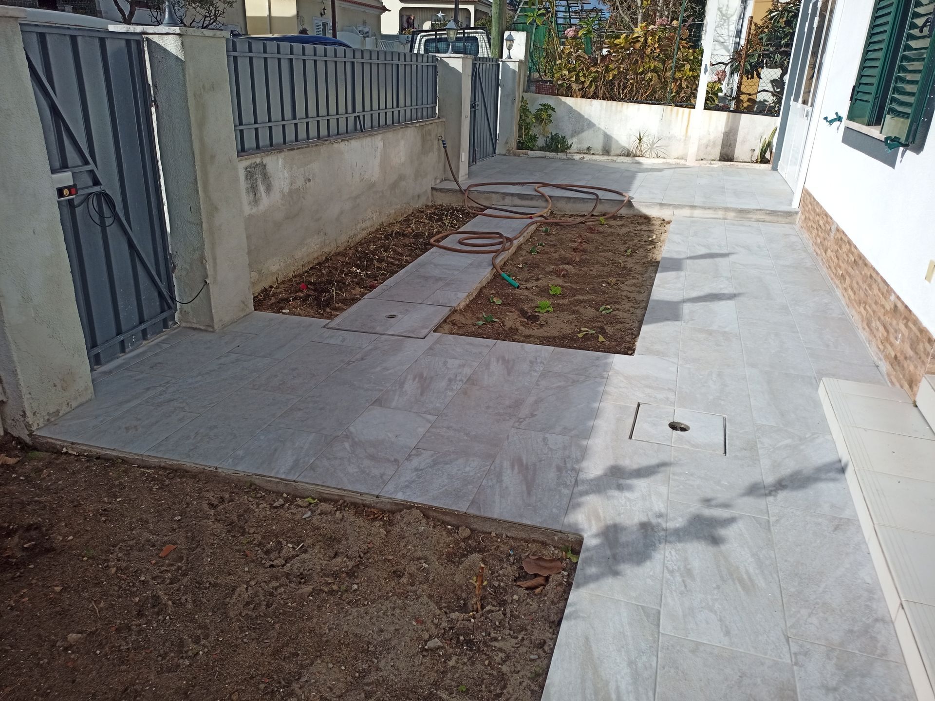 Vista exterior: caminho pavimentado com um canteiro de jardim ao longo de uma cerca e da parede da casa.