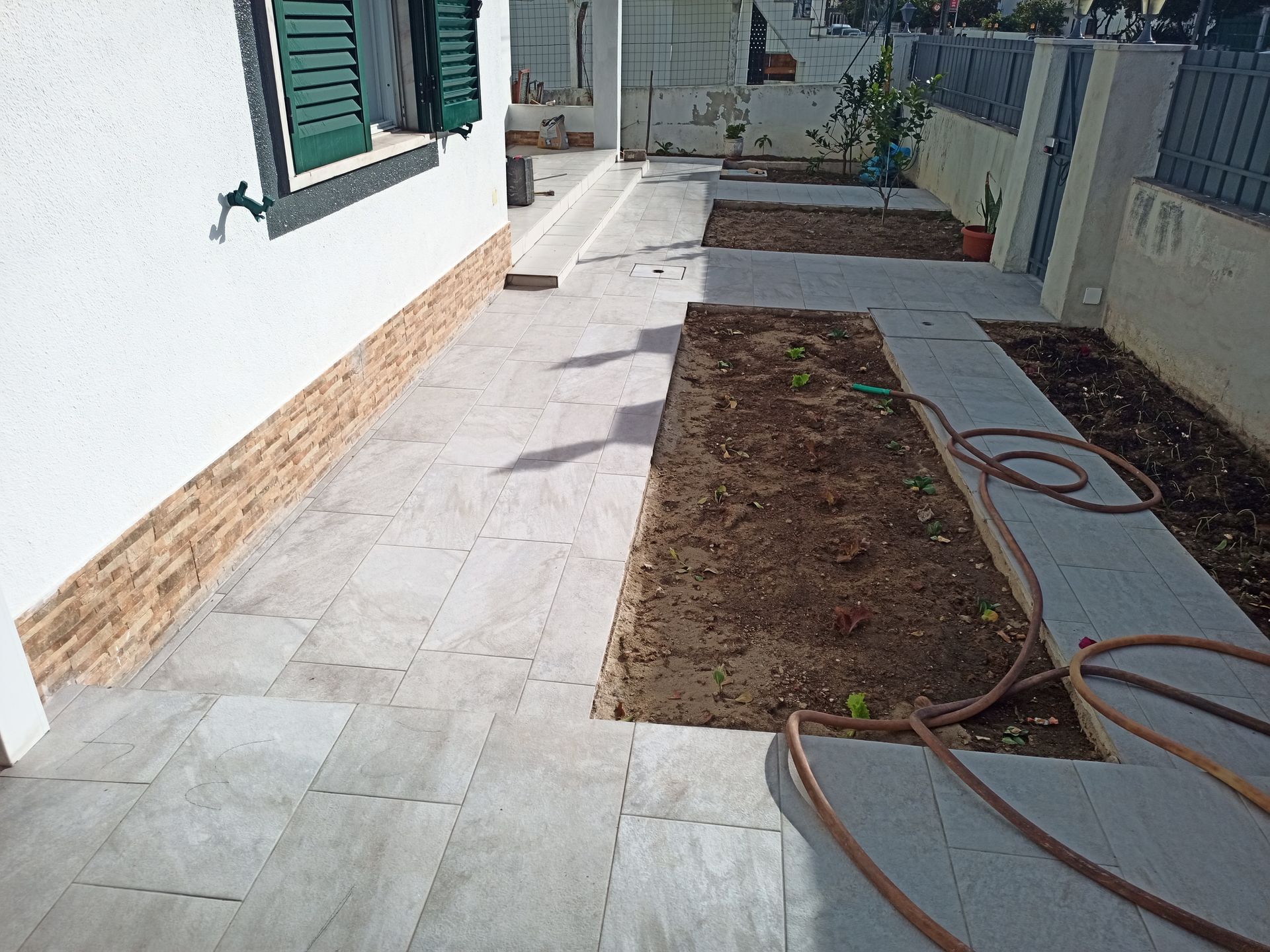 Pátio de pedra com canteiros elevados e uma casa.