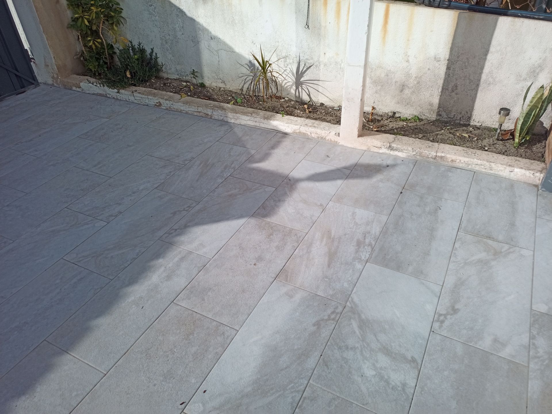 Pátio de pedra com longas sombras projetadas por um edifício ou estrutura.