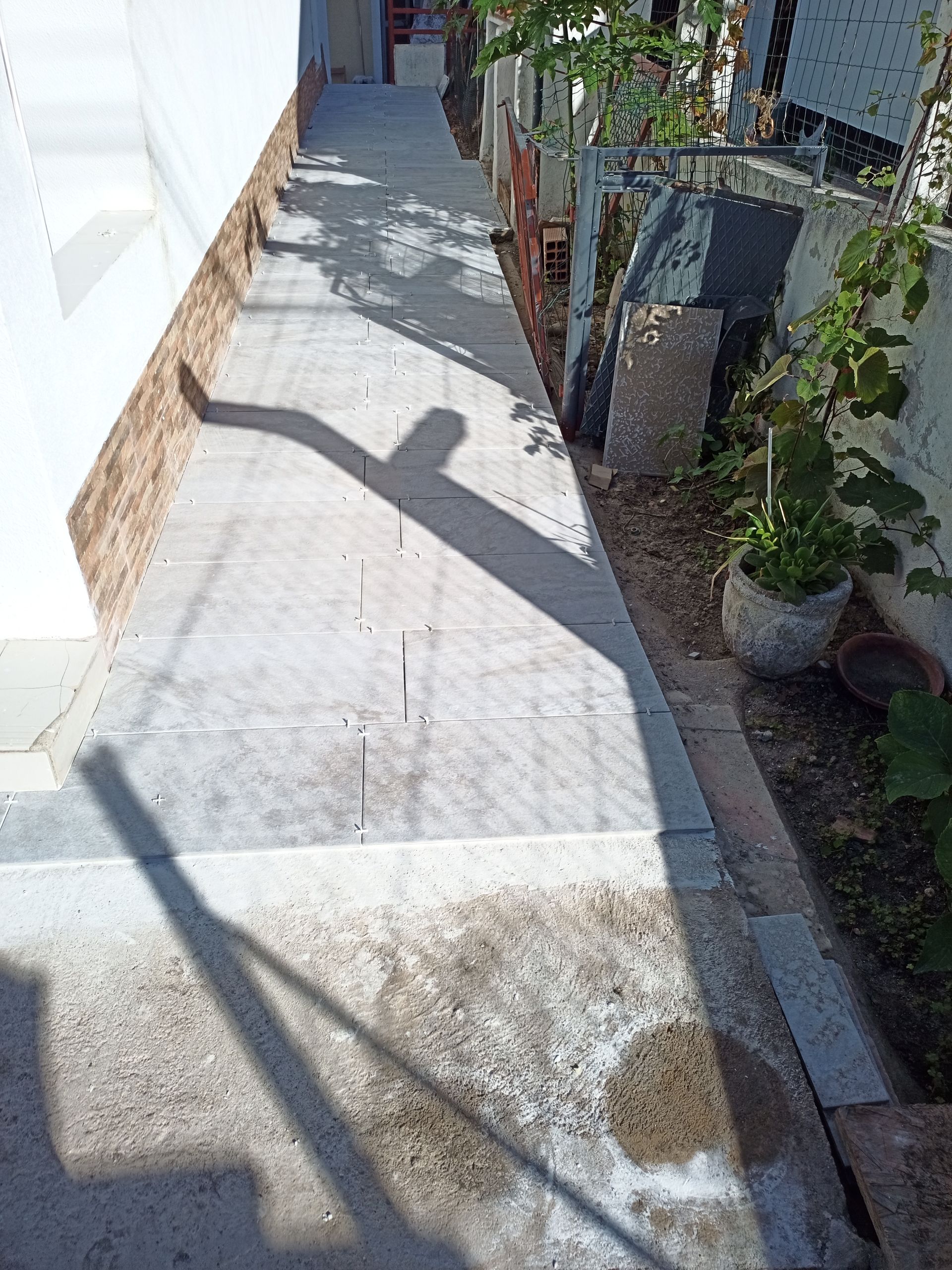 Passarela de concreto com sombra e plantas na lateral.