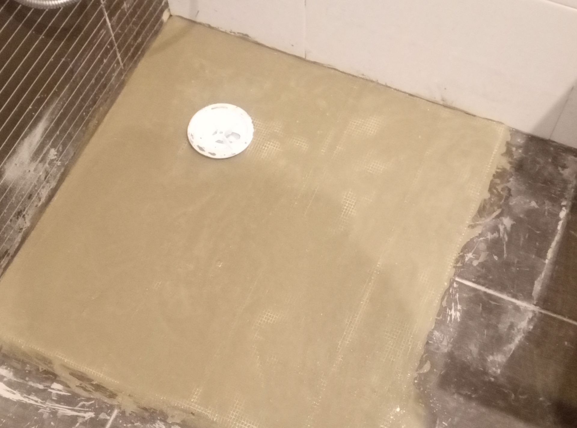 Piso do chuveiro com concreto aparente e tampa de ralo. Azulejos delimitam a área molhada.