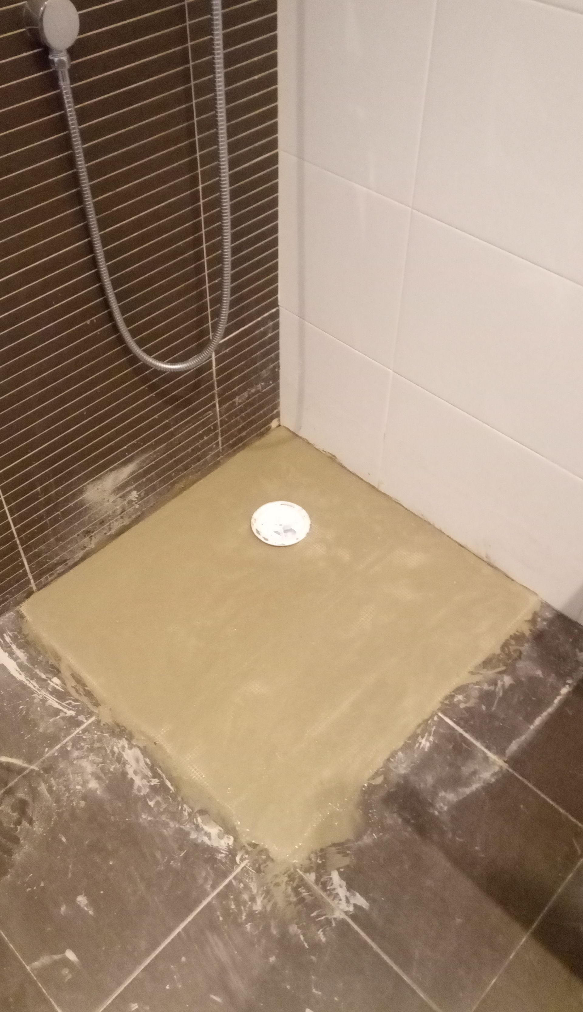 Base de chuveiro com cimento novo ao redor do ralo, revestida com azulejos marrons escuros e brancos.