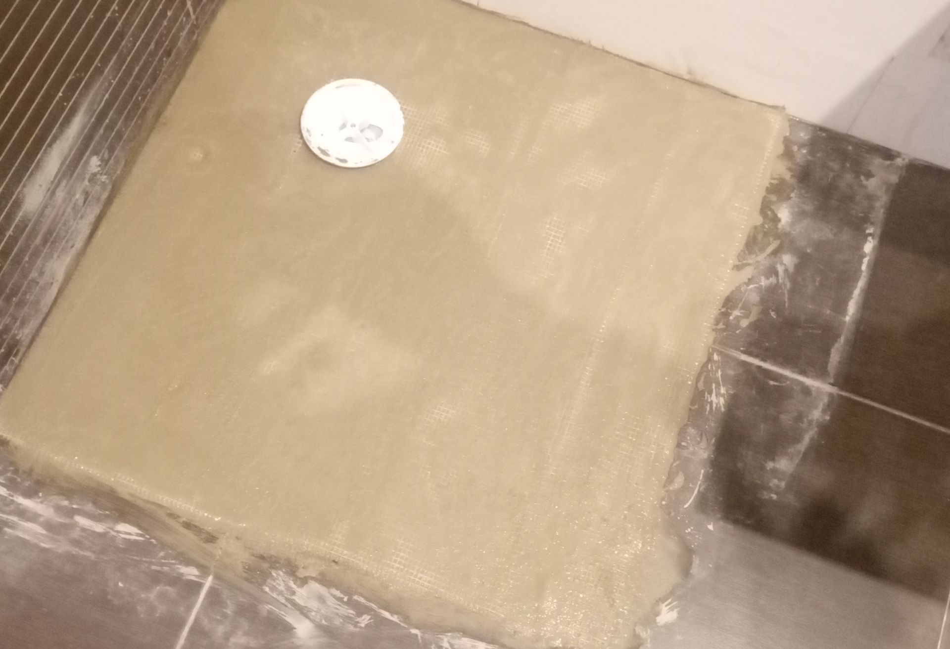 Base do chuveiro com selante para piso molhado, ralo visível. Revestimento de azulejos nas paredes e no piso.