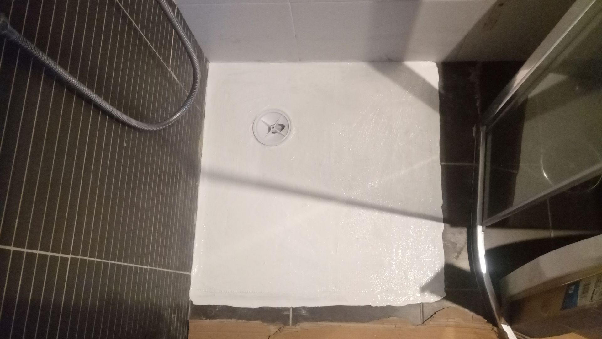 Chuveiro com paredes pintadas de branco e azulejos escuros de um lado; o chuveiro está visível.