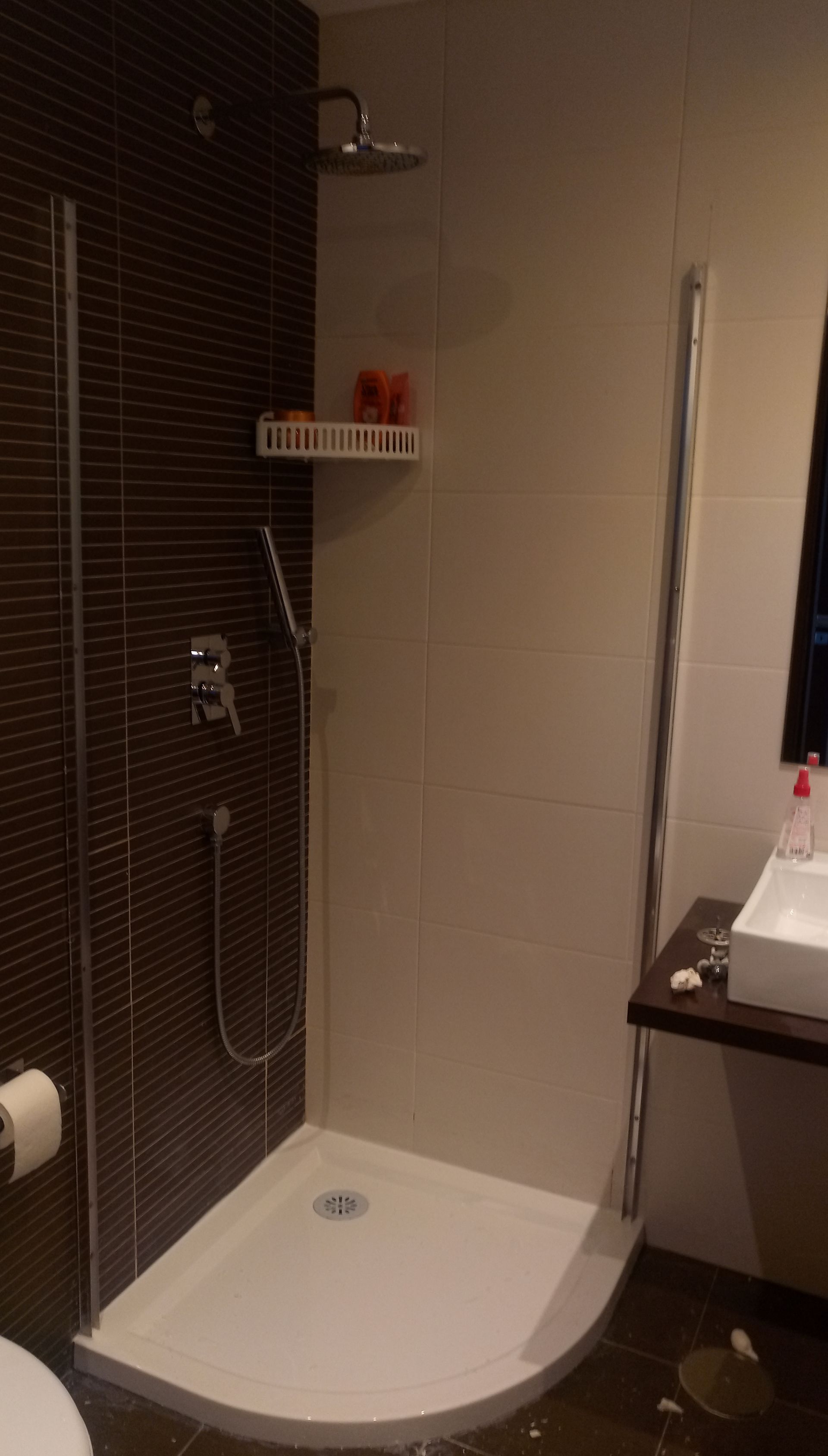 Cabine de duche com base curva branca, parede revestida a azulejos castanhos e porta de vidro.