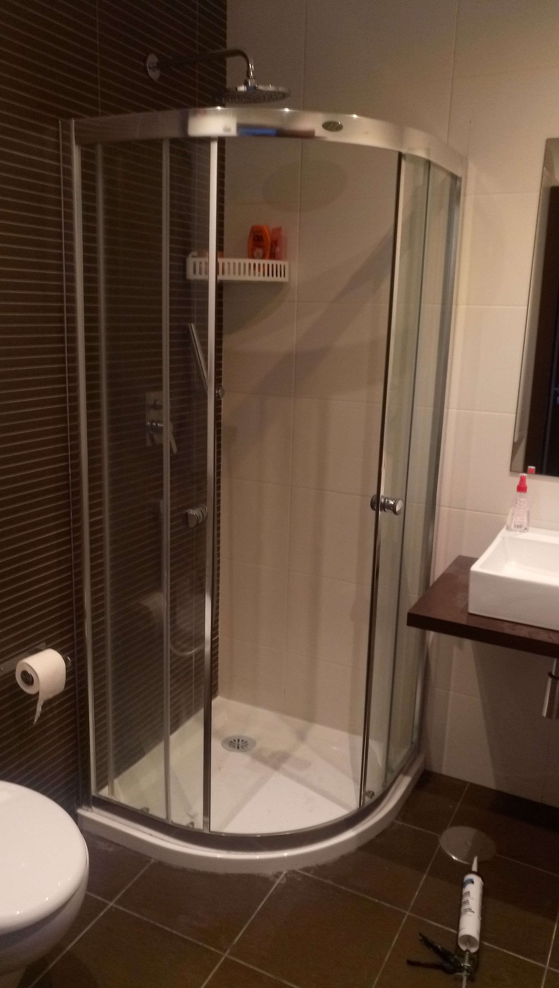 Box de canto com portas de vidro curvas no banheiro. Vaso sanitário e pia visíveis.