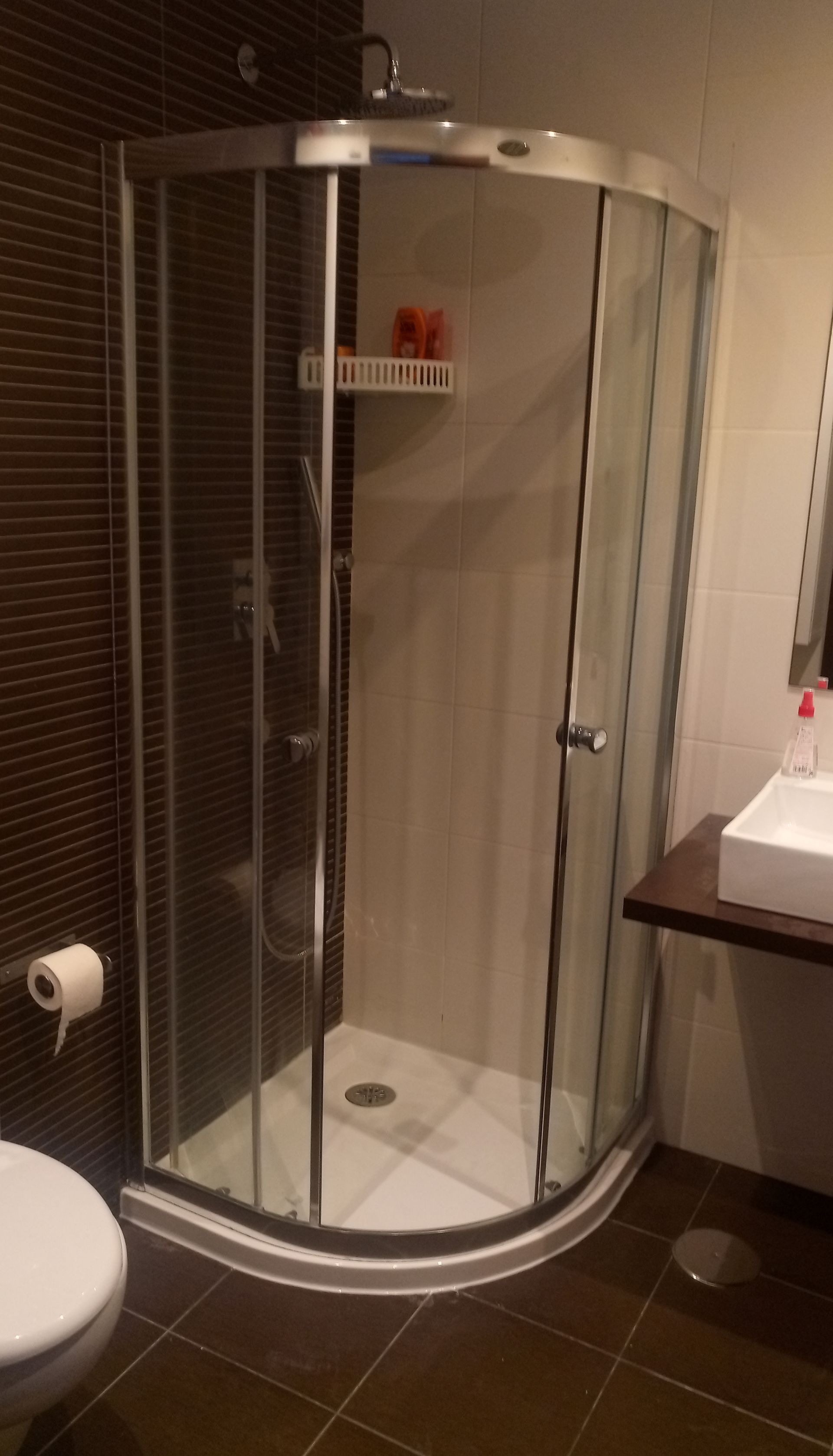 Box de canto com portas de vidro em um banheiro ao lado do vaso sanitário.