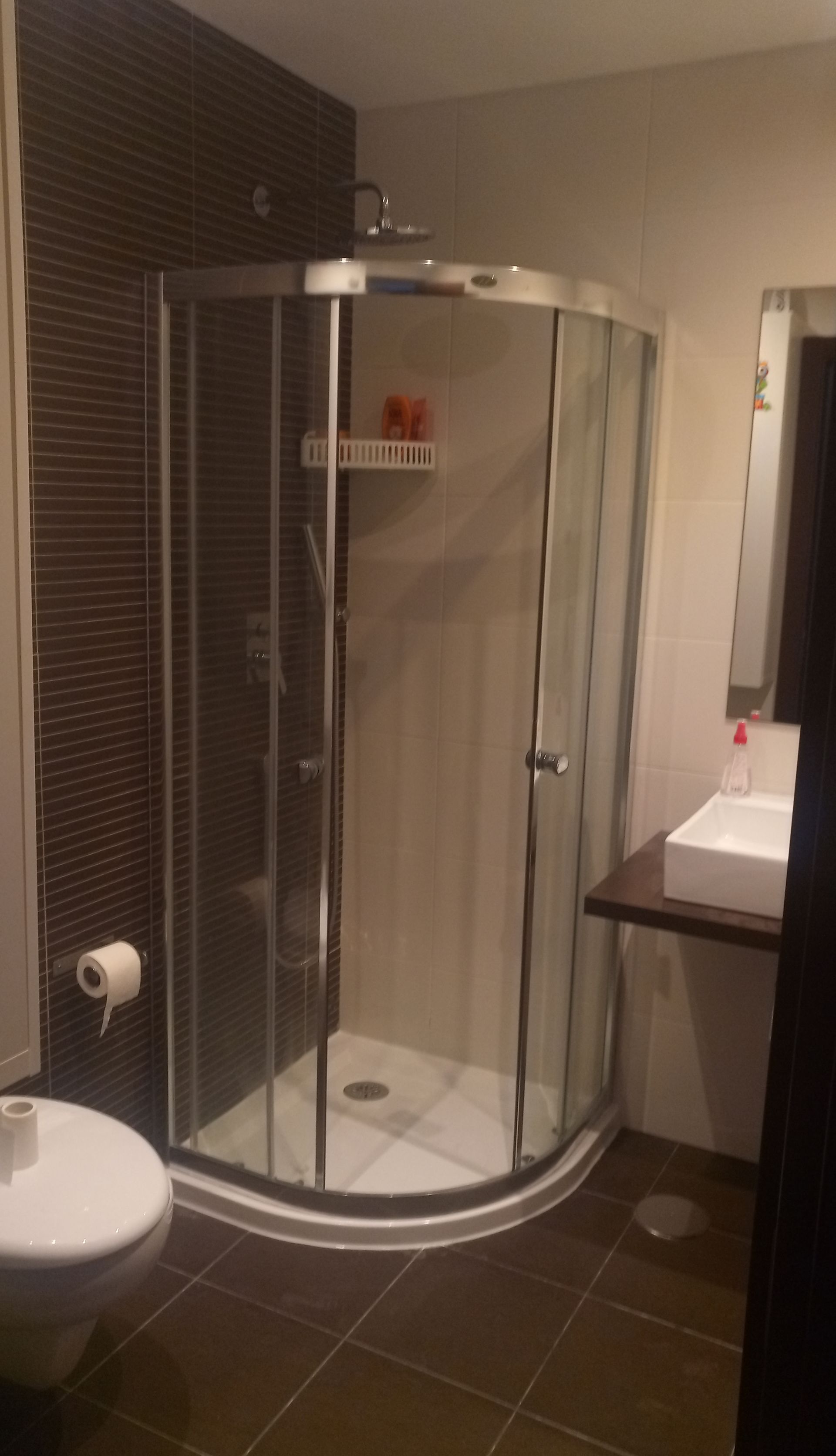 Banheiro com box de canto, vaso sanitário e pia. Azulejos e parede em tom marrom escuro.