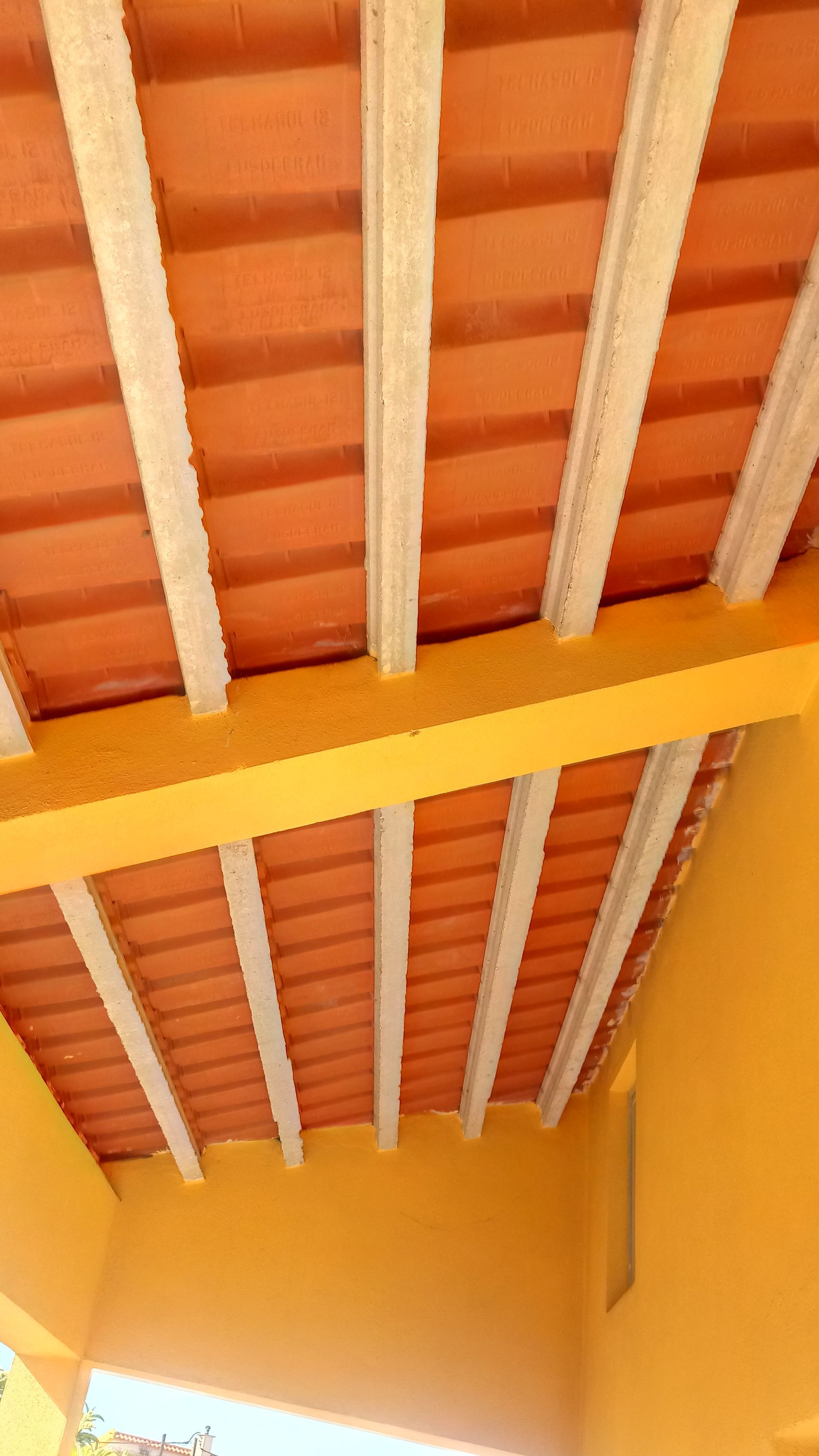 Teto com azulejos laranja e suportes brancos, sustentado por uma viga amarela.