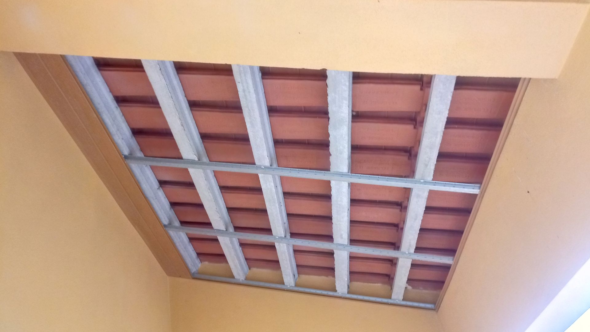 Teto com telhas de barro vermelho sustentadas por vigas cinzentas e emoldurado por uma borda marrom.