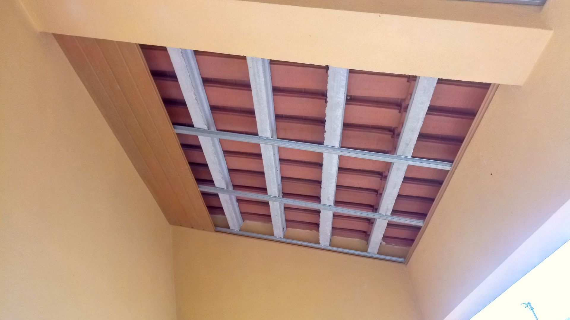 Telhas vermelhas sustentadas por vigas de metal, embutidas em um teto pintado de amarelo.