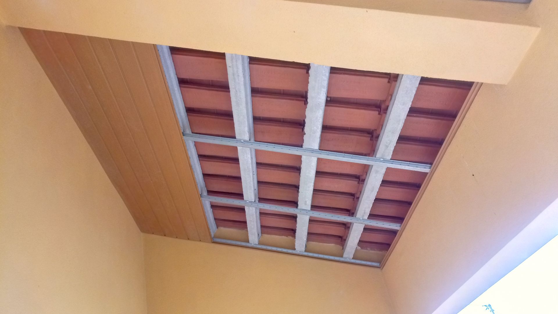 Teto com tijolos aparentes, suportes metálicos e painéis de madeira na lateral. Cores laranja e bege.