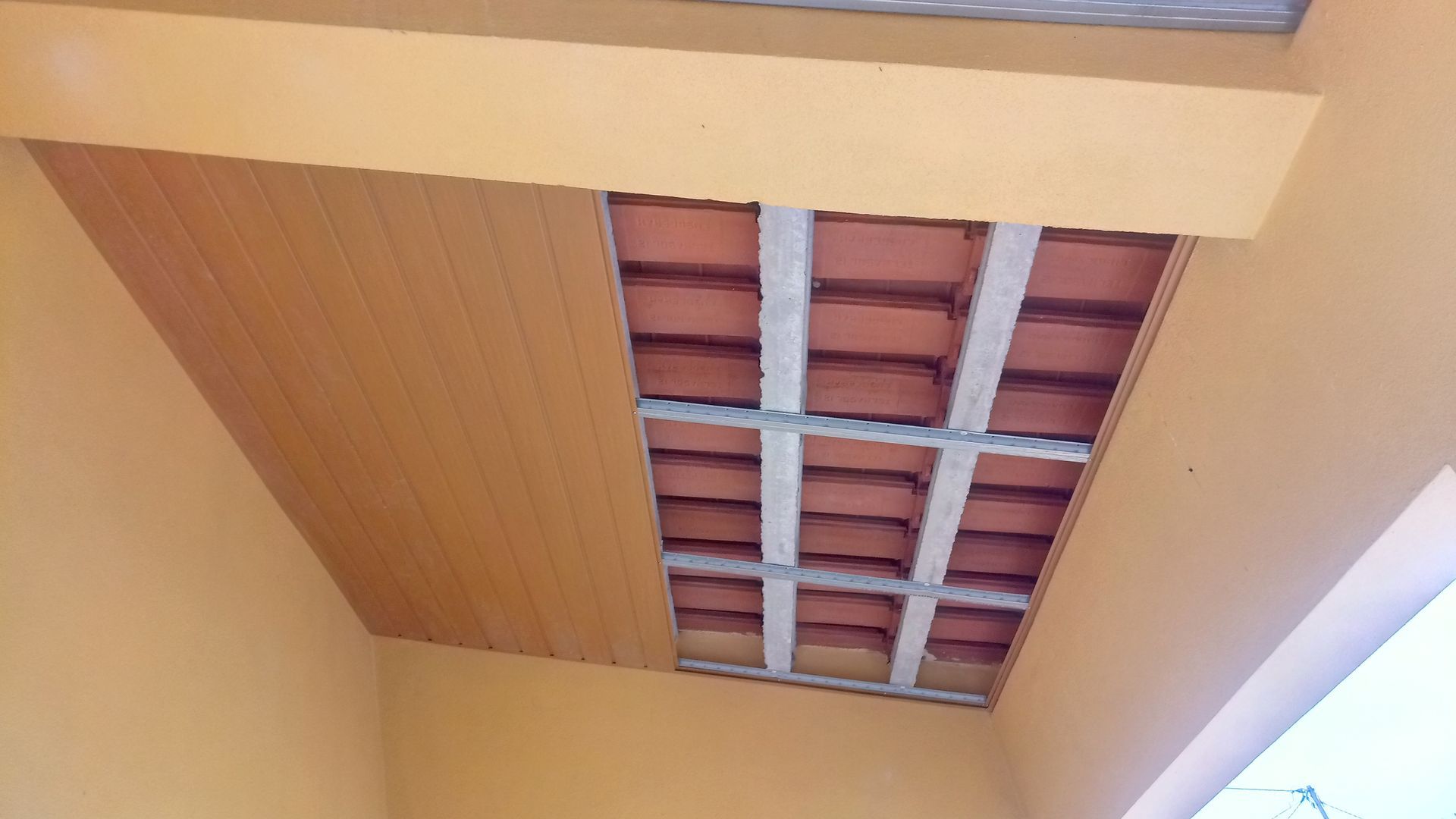 Teto parcialmente instalado com tijolos vermelhos aparentes e painéis de madeira.