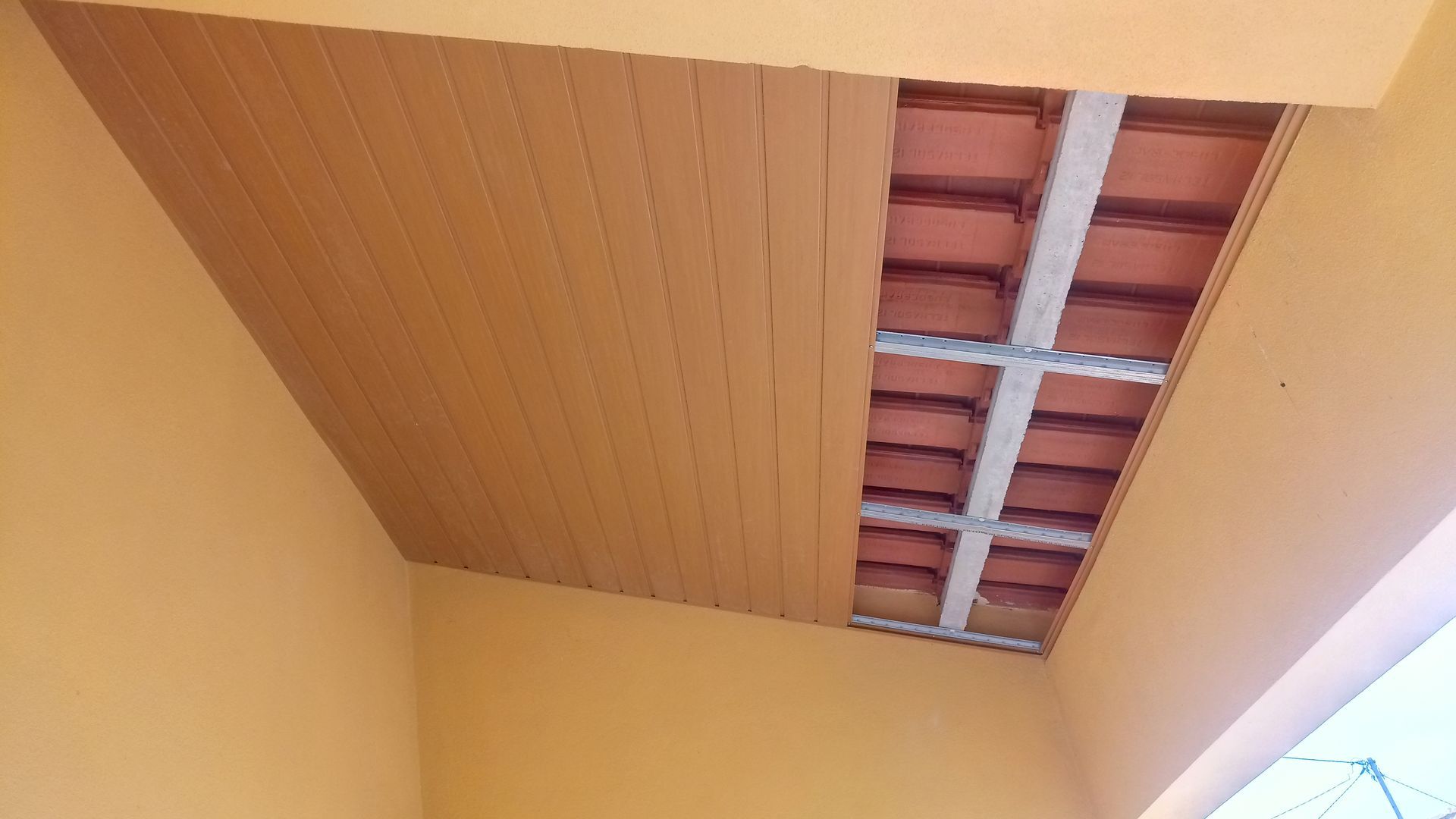 Estrutura do teto: parcialmente revestido com painéis de madeira, telhas de barro aparentes e vigas de concreto. Paredes laranja.