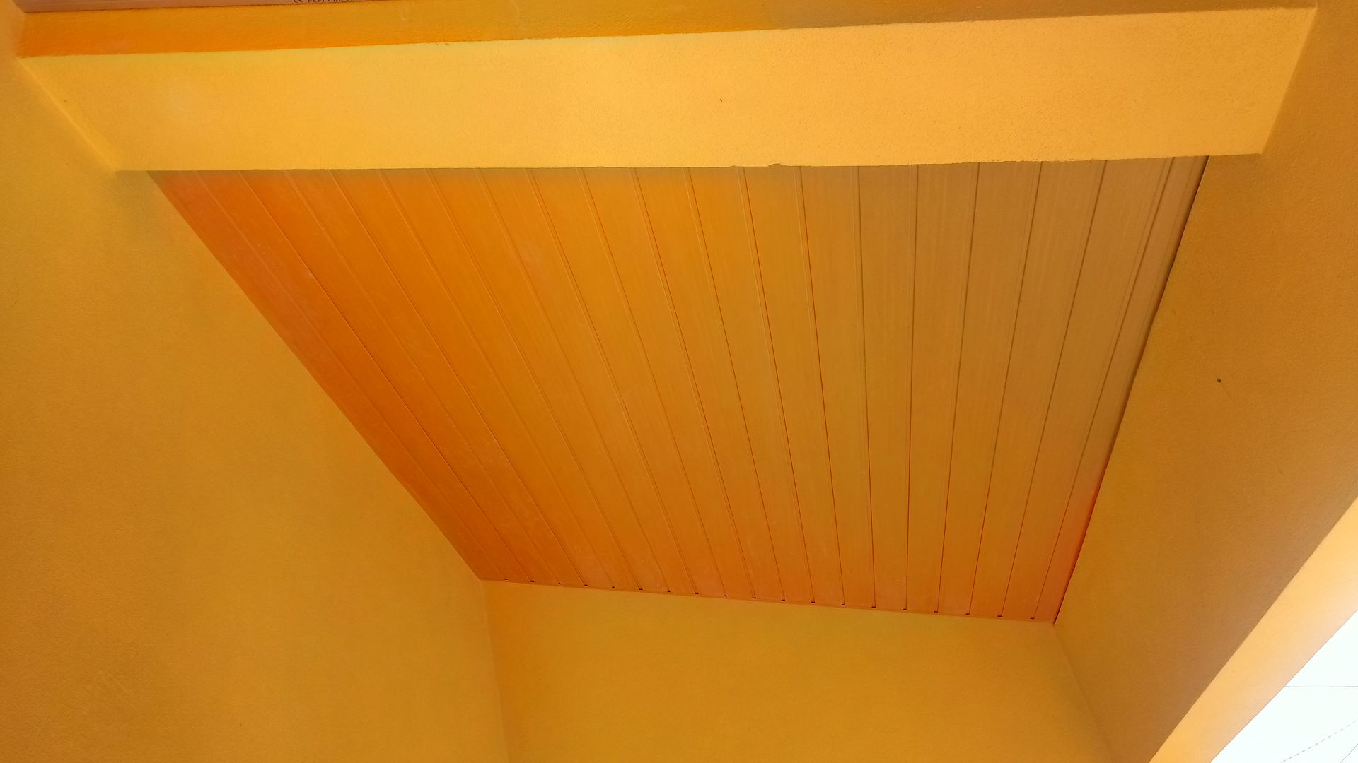 Teto de madeira amarelo e laranja com viga horizontal, parede inclinada.
