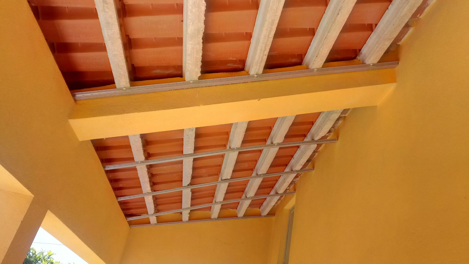 Teto laranja com telhas de terracota e vigas brancas, visto de baixo em um quarto amarelo.