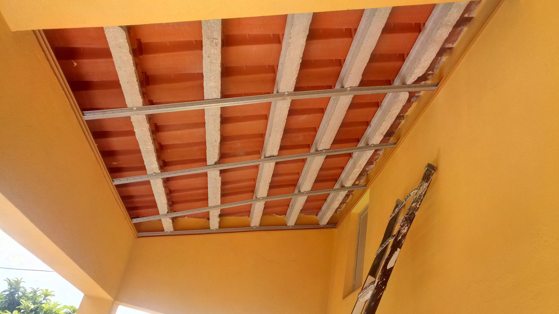 Teto com azulejos laranja e vigas brancas, em contraste com uma parede laranja.