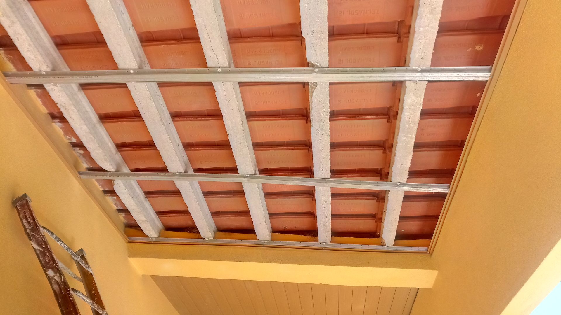 Telhado de telha laranja sustentado por vigas brancas e estrutura metálica.