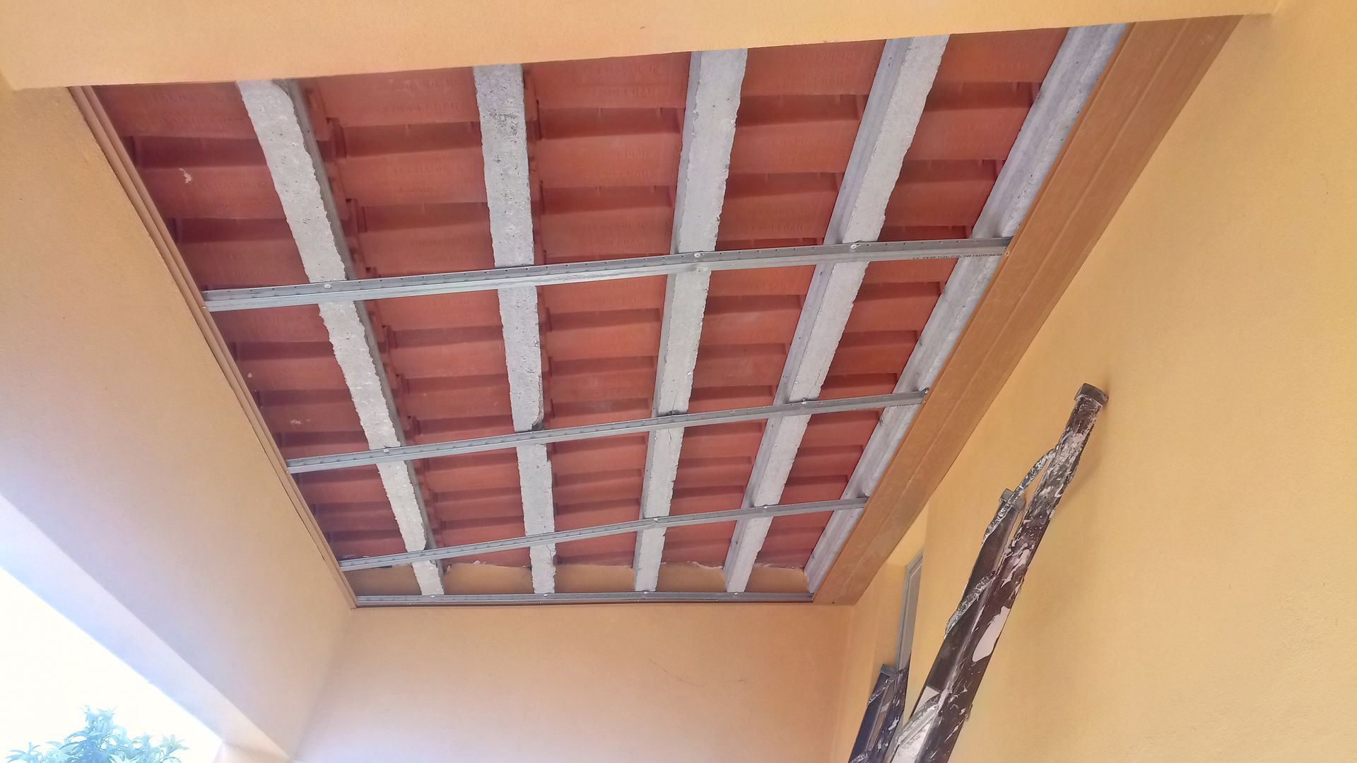 Vista aérea de um teto de telhas de terracota sustentado por vigas de metal dentro de uma estrutura de paredes amarelas.