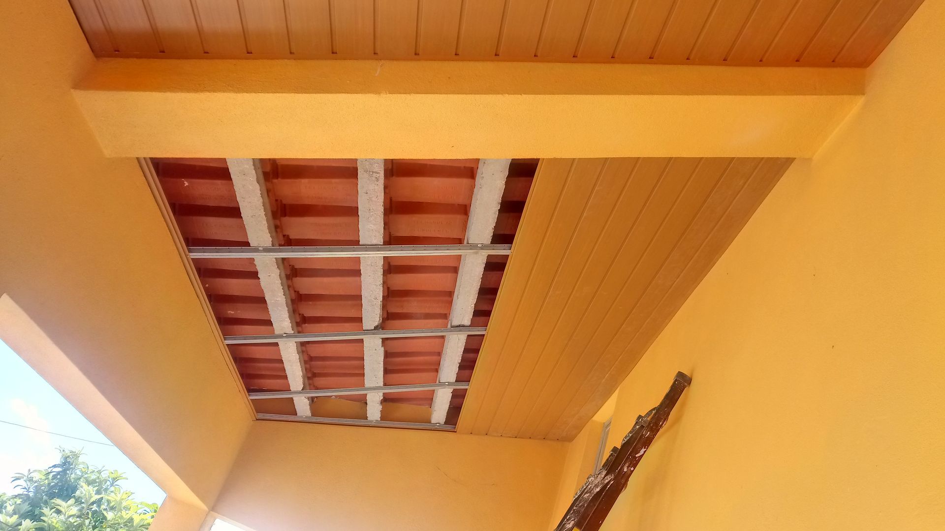 Teto laranja com azulejos vermelhos visíveis e vigas de sustentação aparentes; uma parte possui painéis de madeira.