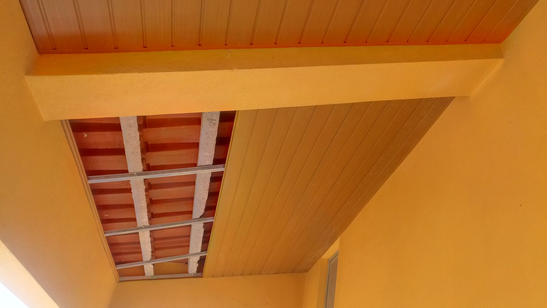 Teto interior laranja com tijolos aparentes, vigas metálicas e painéis de madeira.