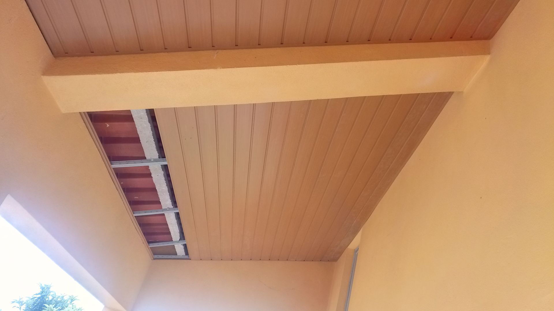 Teto de madeira marrom-claro com uma viga horizontal, instalado em uma varanda externa.