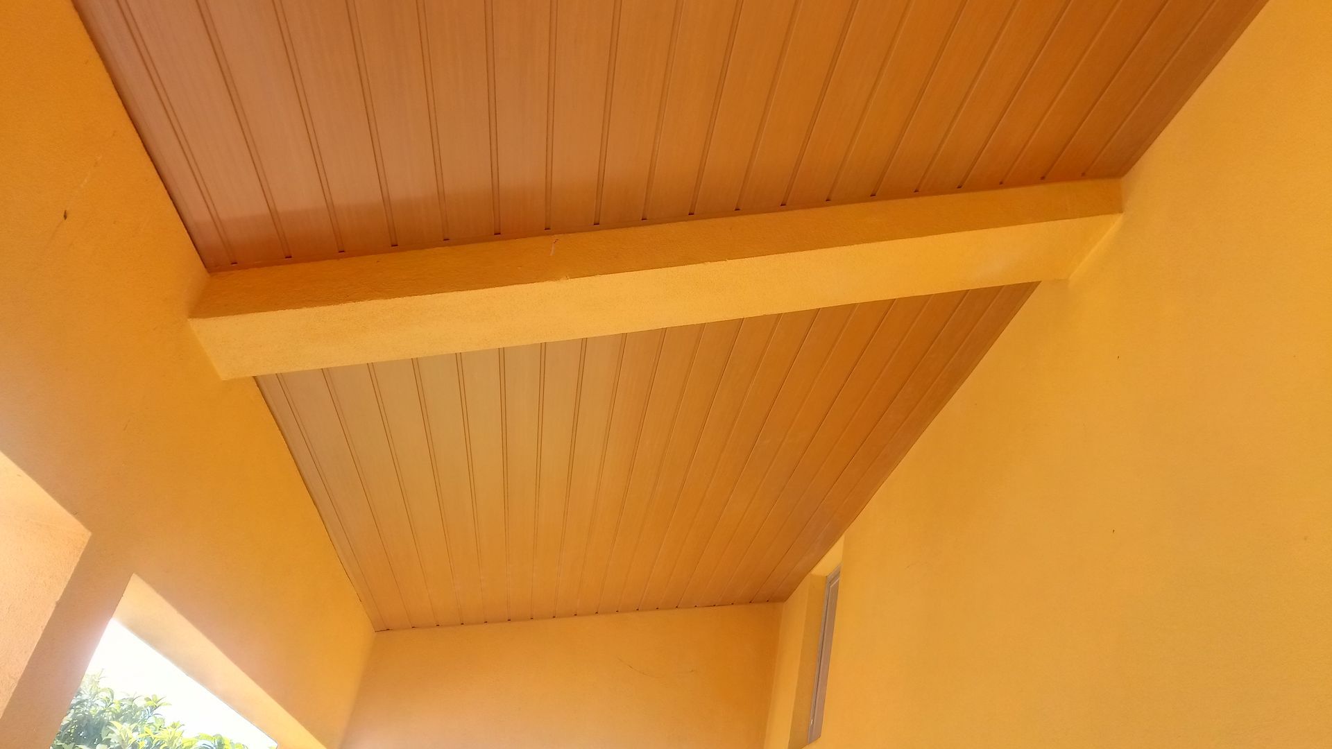Teto amarelo com painéis imitando madeira e uma viga de sustentação, inserido em uma estrutura amarela.