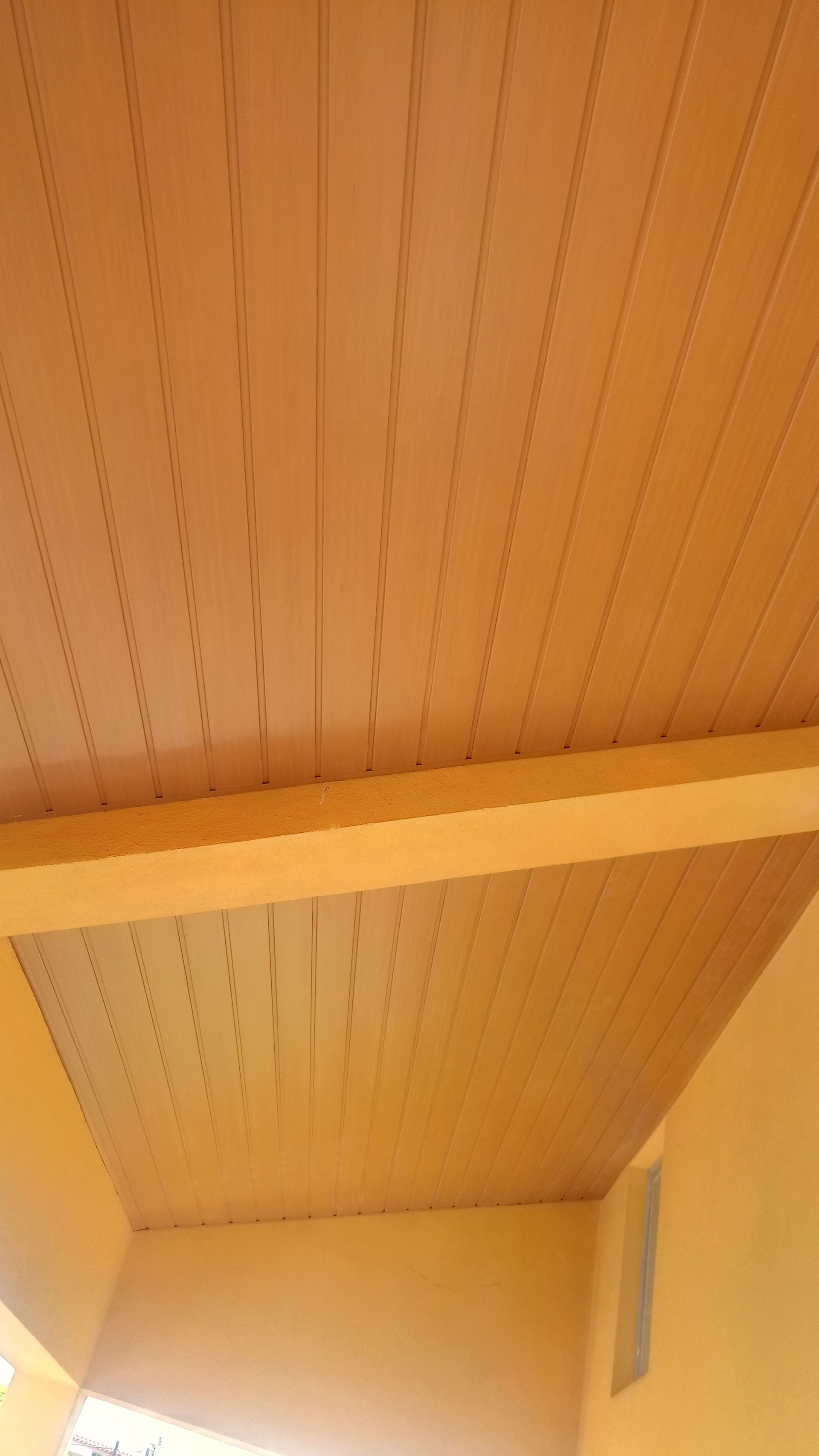 Teto e paredes revestidos com tábuas de madeira bege, com viga de sustentação.