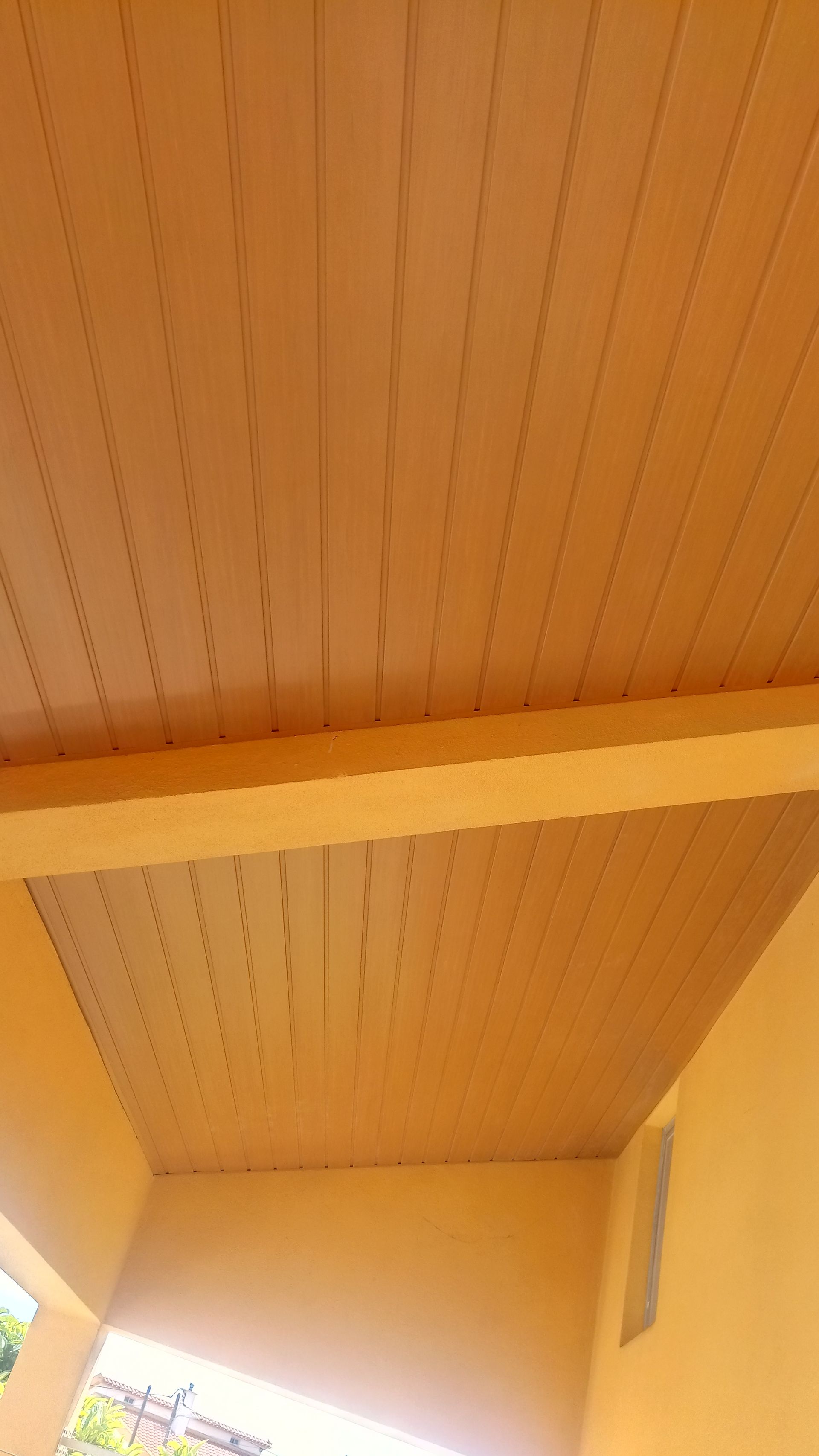 Teto ripado de madeira com viga de sustentação, pintado de castanho claro.