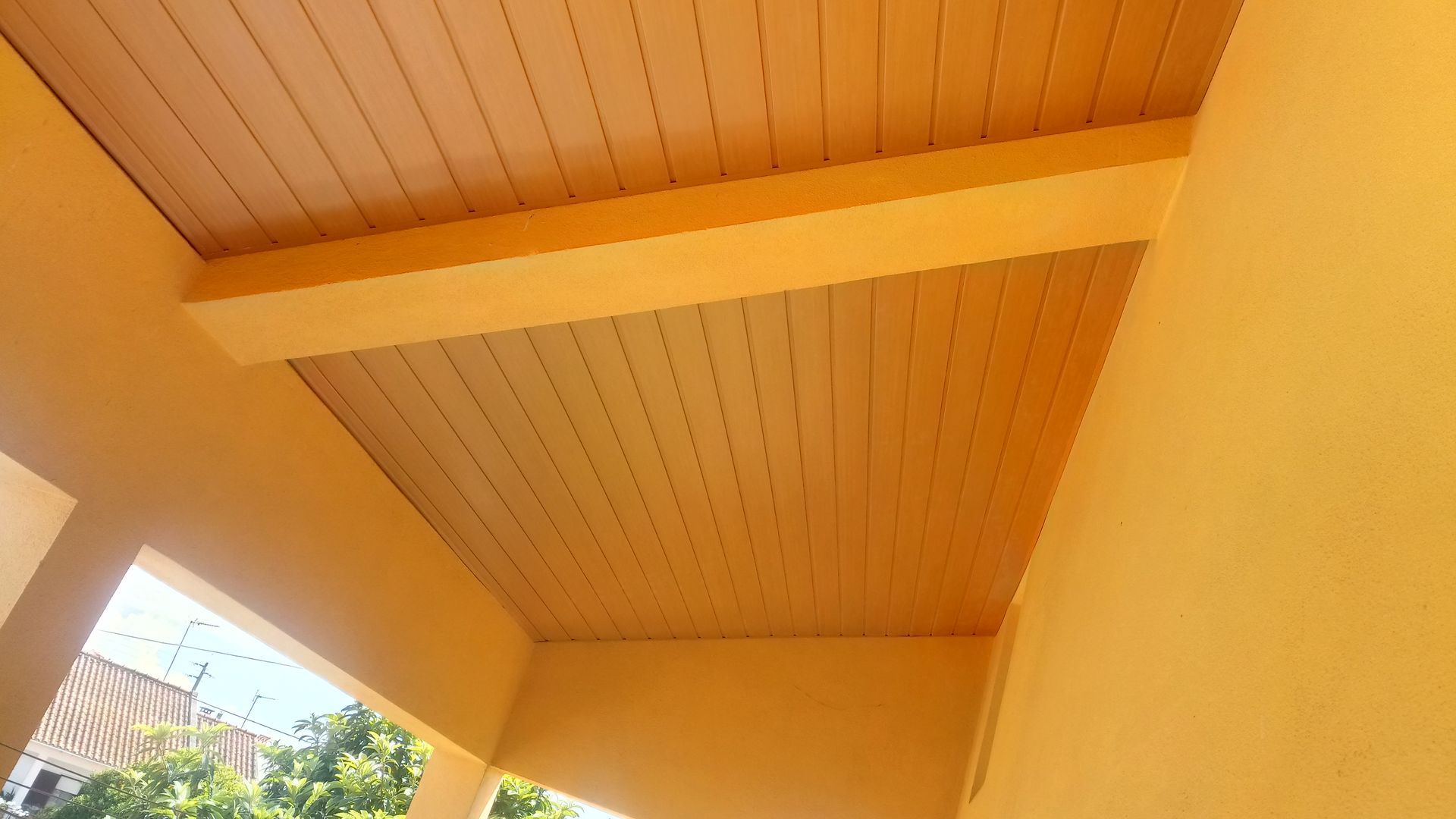 Teto pintado de amarelo com tábuas de madeira visíveis, vigas aparentes, área externa.