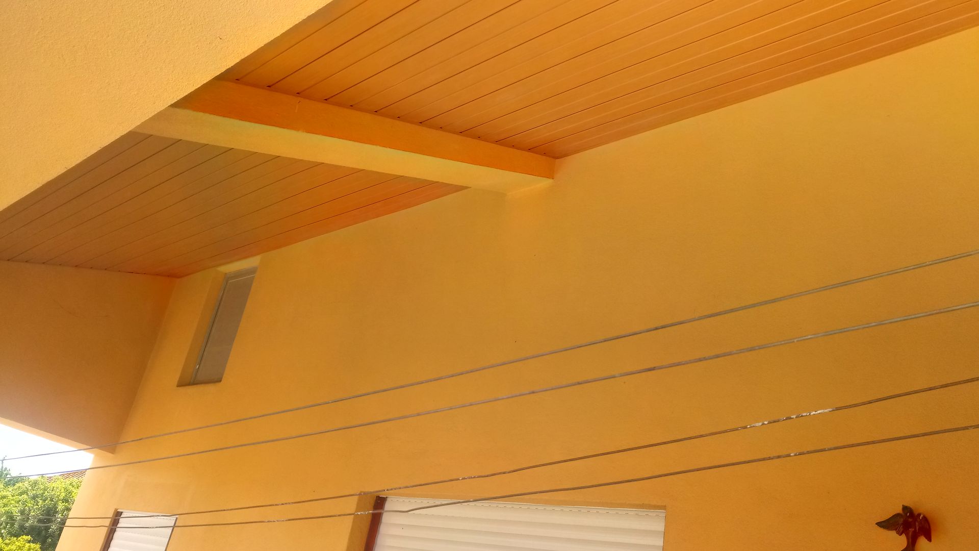 Exterior amarelo com teto ripado laranja, janela e varal de roupas.
