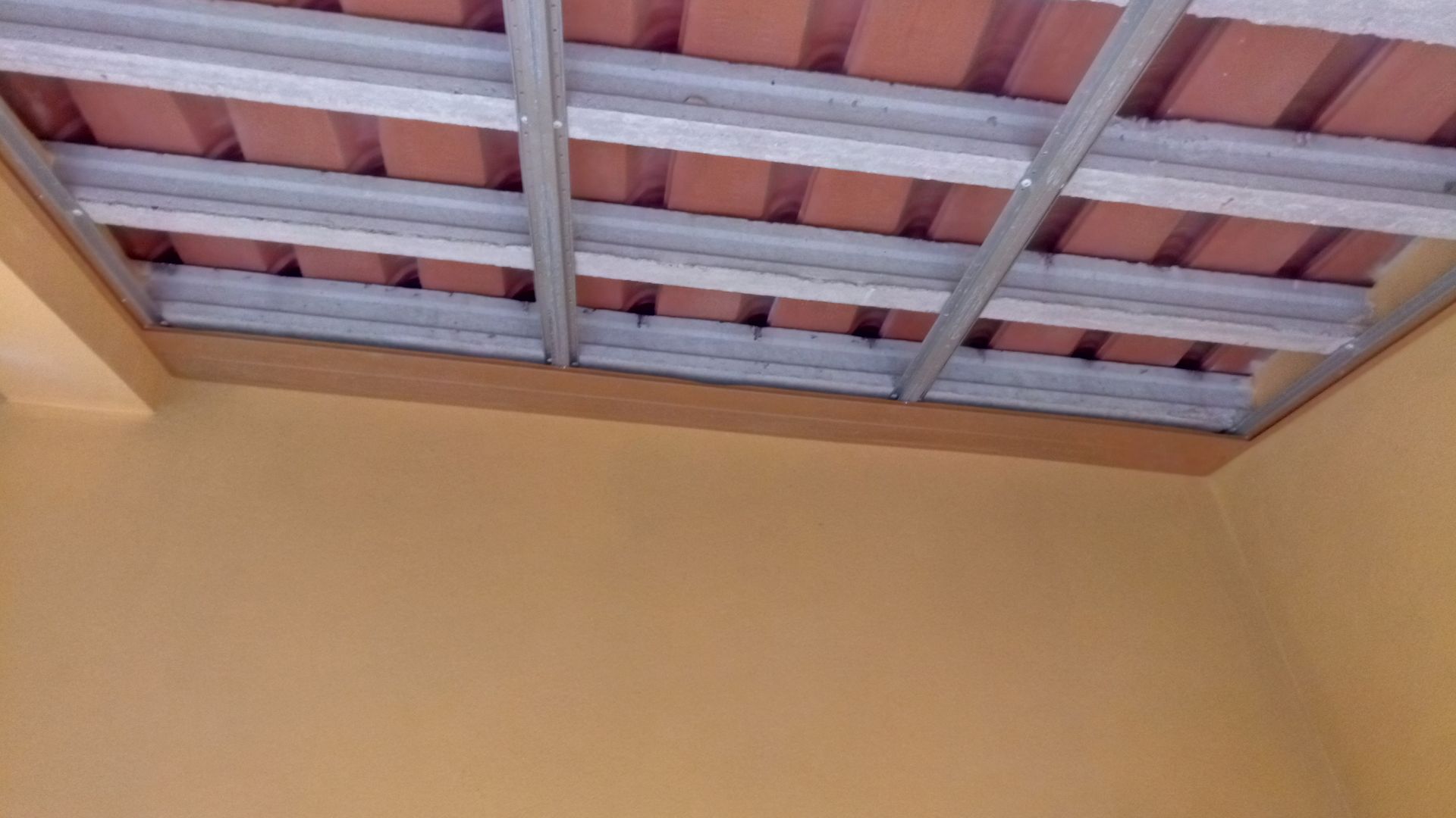 Vista da estrutura exposta do teto com vigas de metal e telhas de barro vermelho.