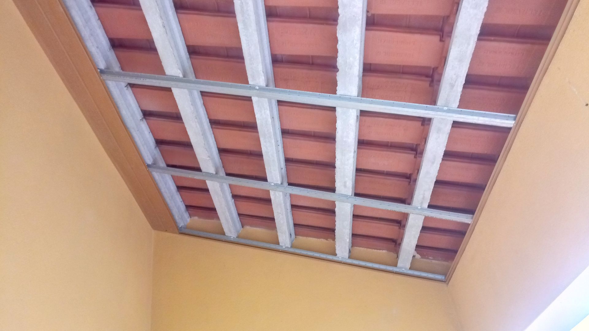 Estrutura do teto com telhas de terracota vermelha sustentadas por vigas brancas e estrutura metálica.