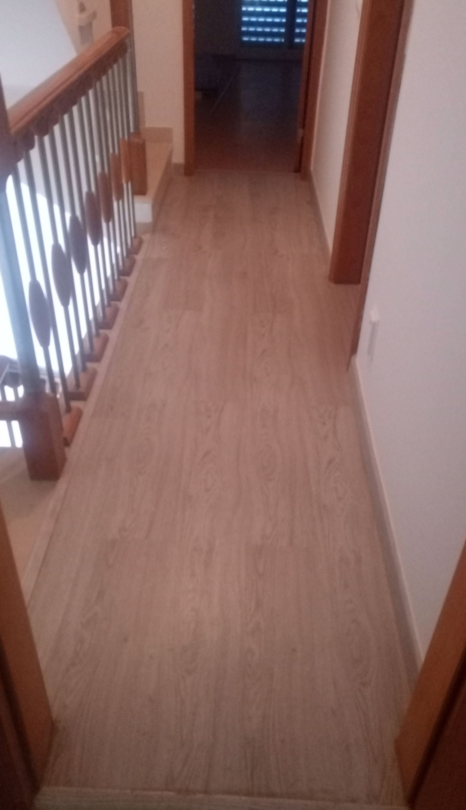 Corredor com piso de madeira clara, uma escada com corrimão de madeira e portas em ambos os lados.