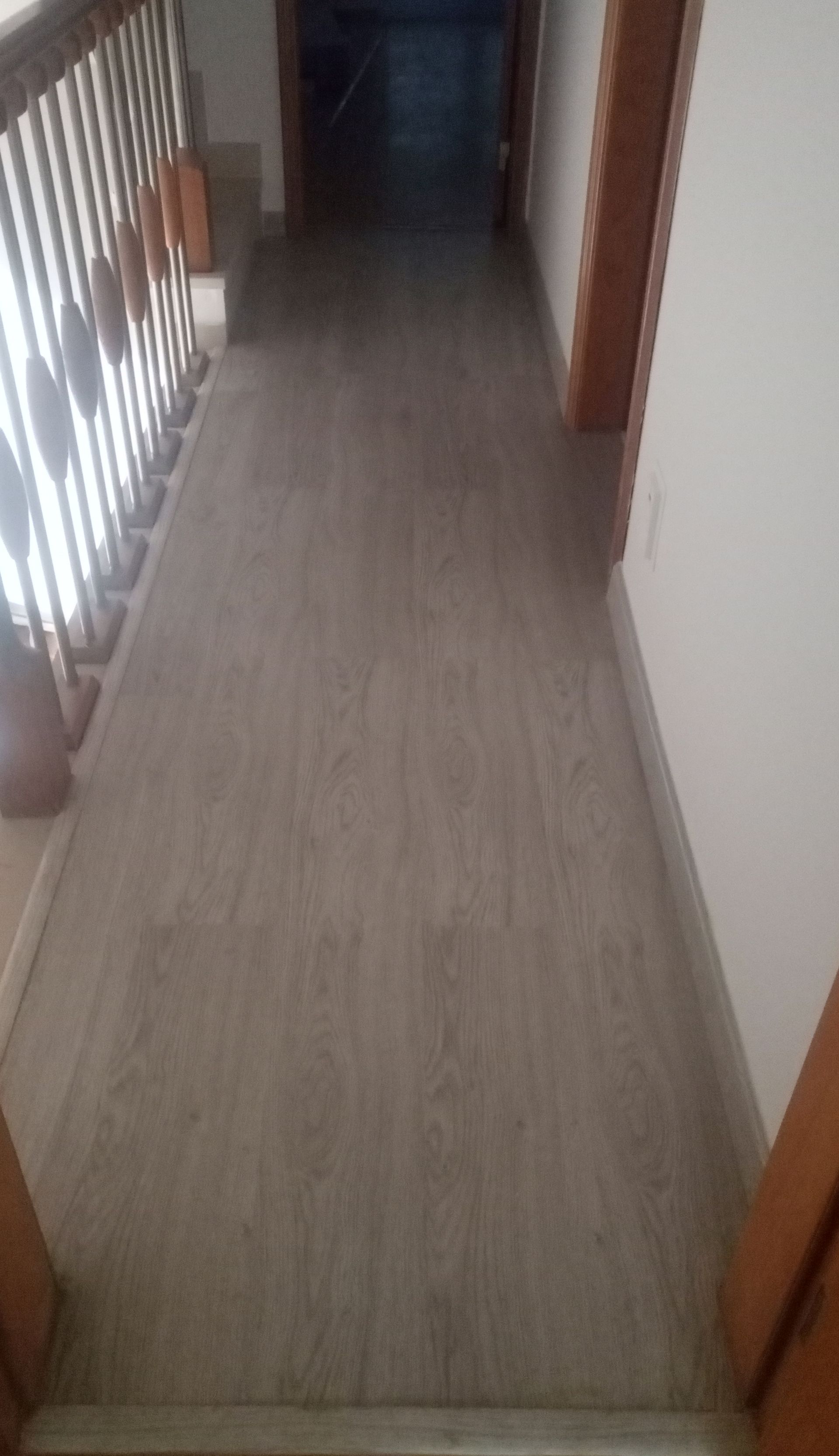 Corredor com piso imitando madeira cinza, escada à esquerda e portas à direita e no final.