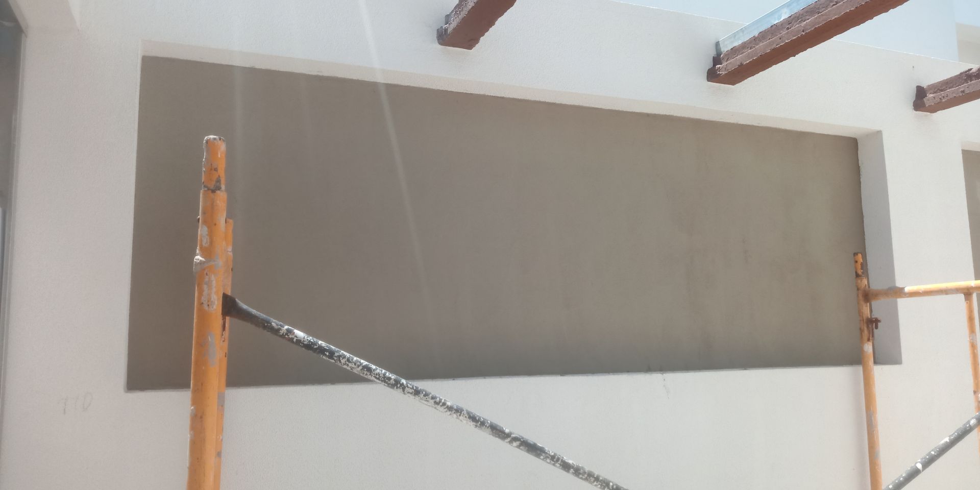 Parede com uma grande abertura retangular cinza, andaimes e vigas de madeira acima.