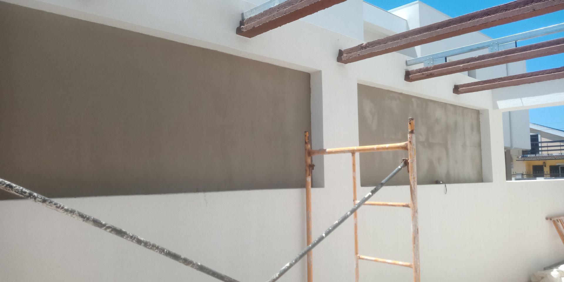 Canteiro de obras: paredes brancas com grandes seções rebaixadas em cinza; andaimes e vigas suspensas.