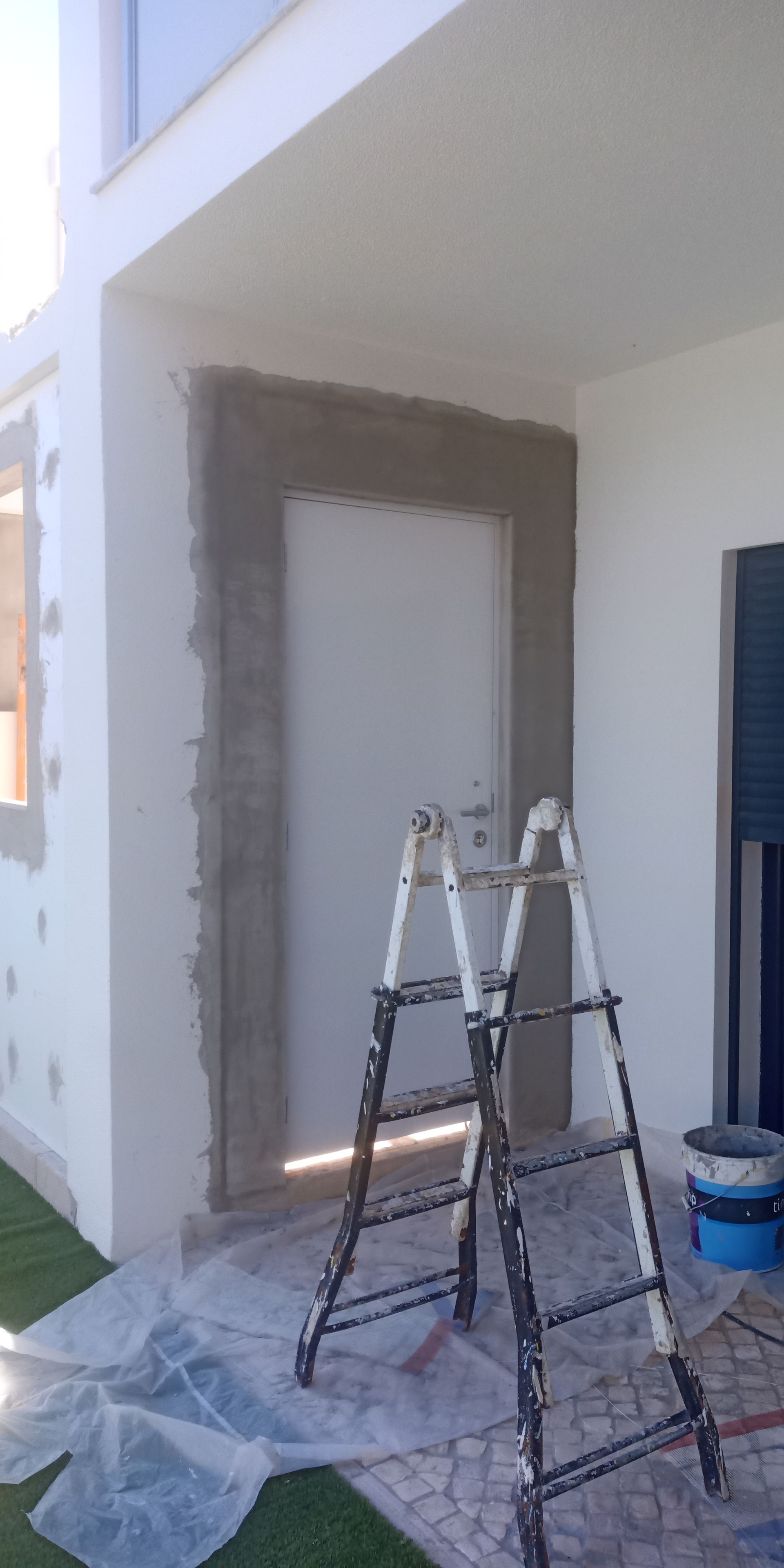 Escada ao lado de uma porta na parte externa de um prédio, cercada por cimento fresco durante a construção.