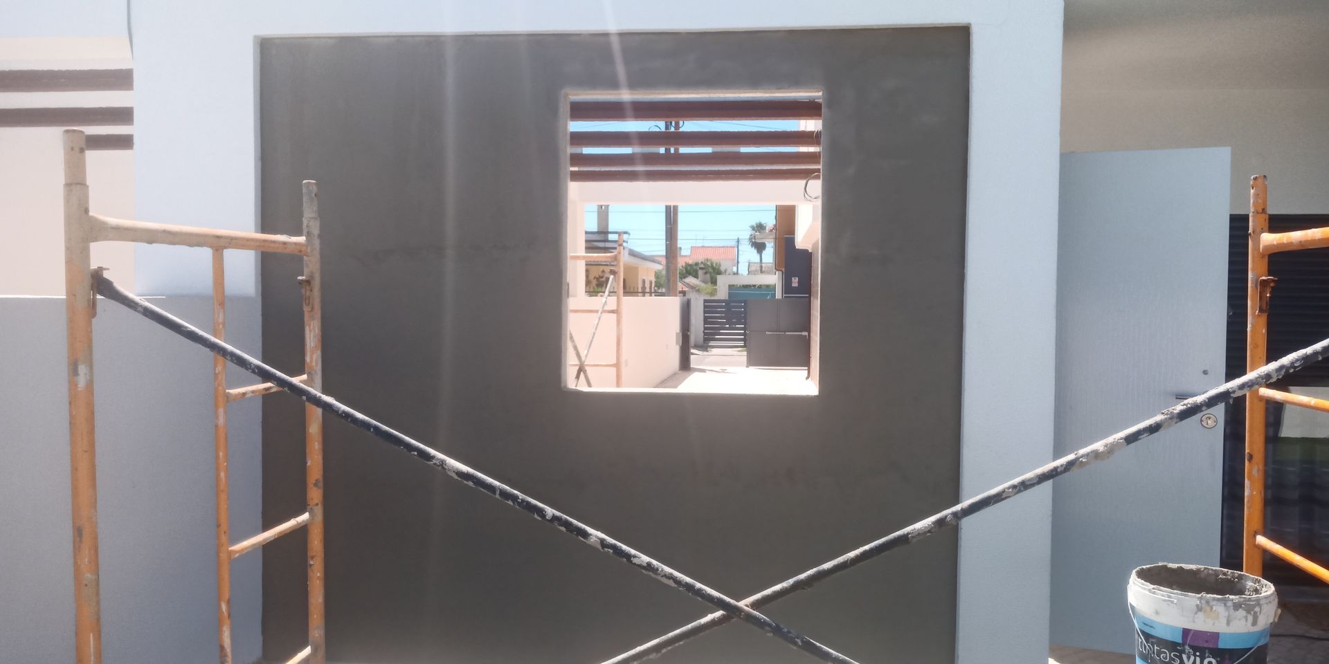 Canteiro de obras com andaimes e uma parede com uma janela. A parede está pintada de cinza escuro.