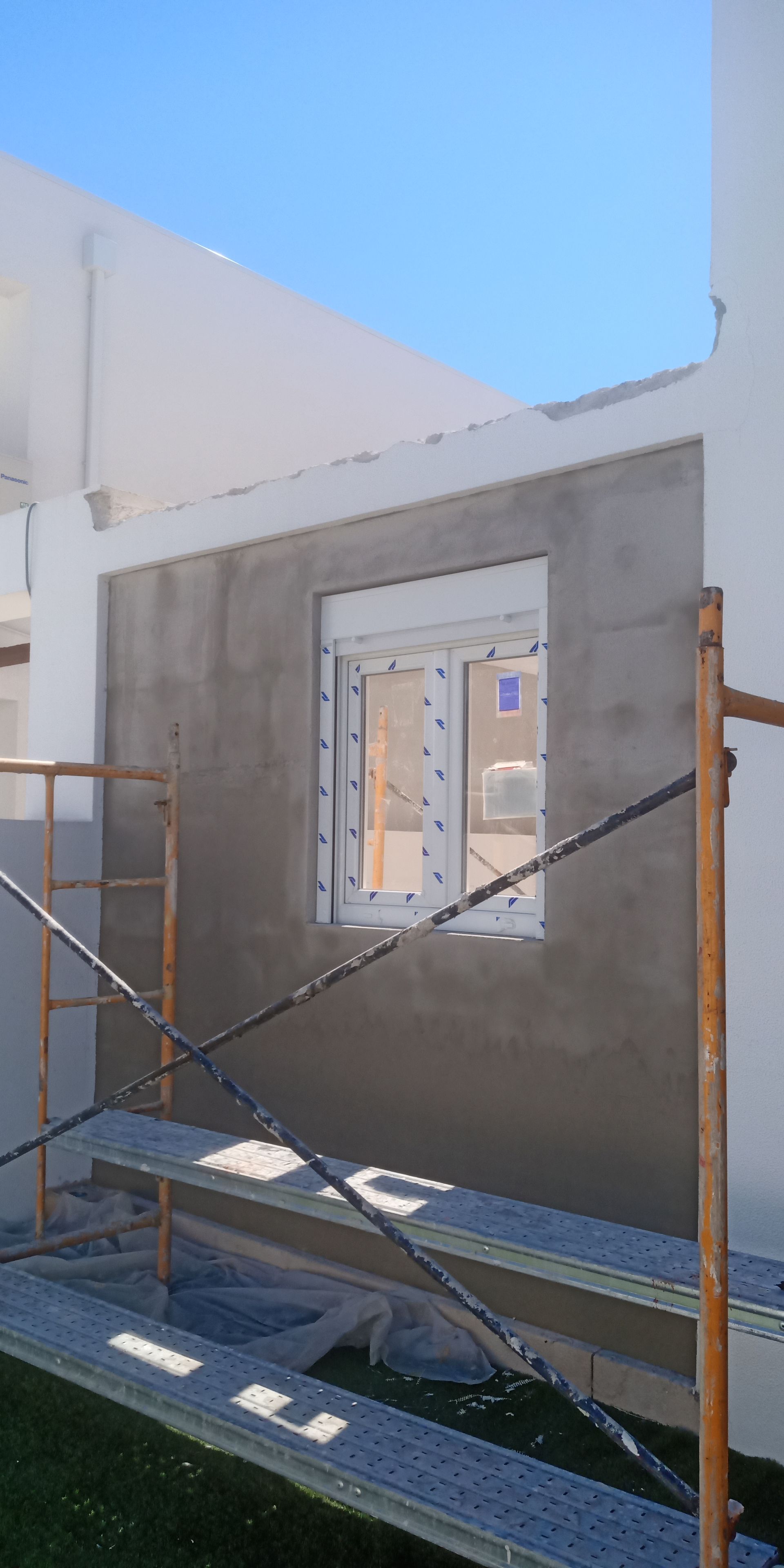 Canteiro de obras com andaimes e uma janela na parede, céu ao fundo.