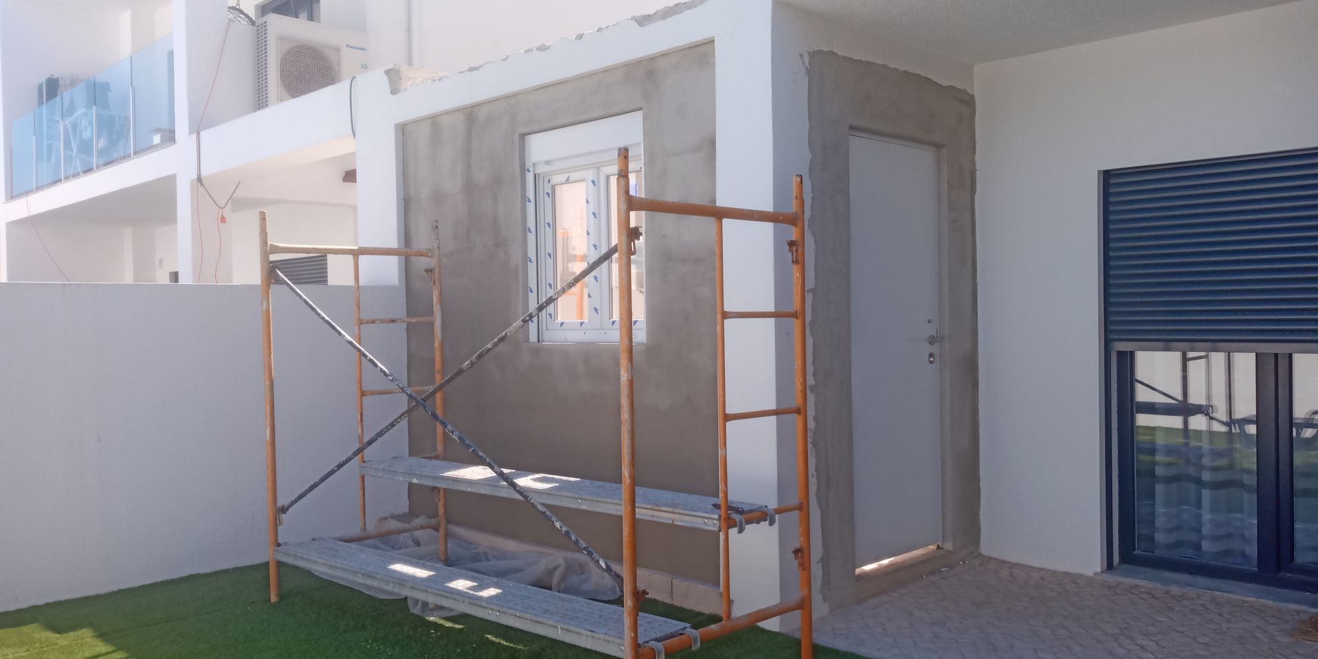 Canteiro de obras: andaimes junto a uma parede com janela, porta e superfície parcialmente acabada.