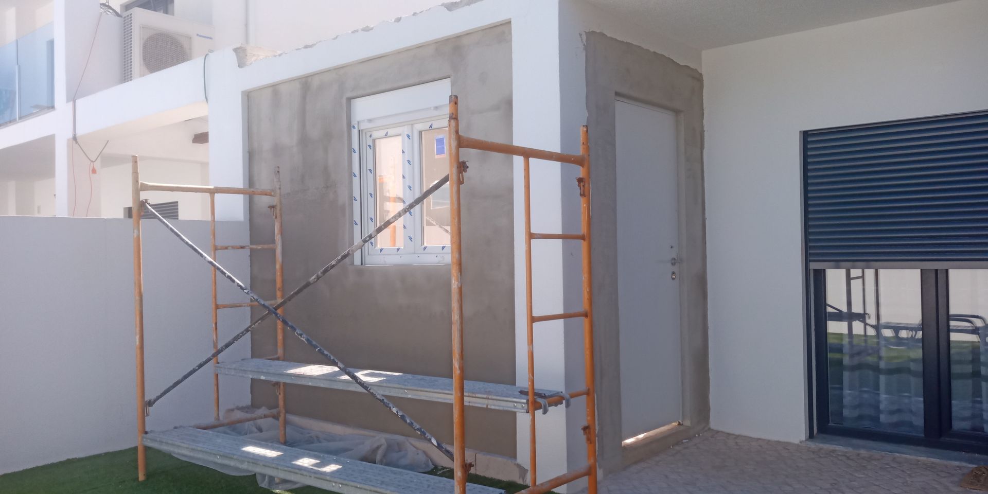 Obra em construção, rebocando parede externa com janela e porta, com andaimes.