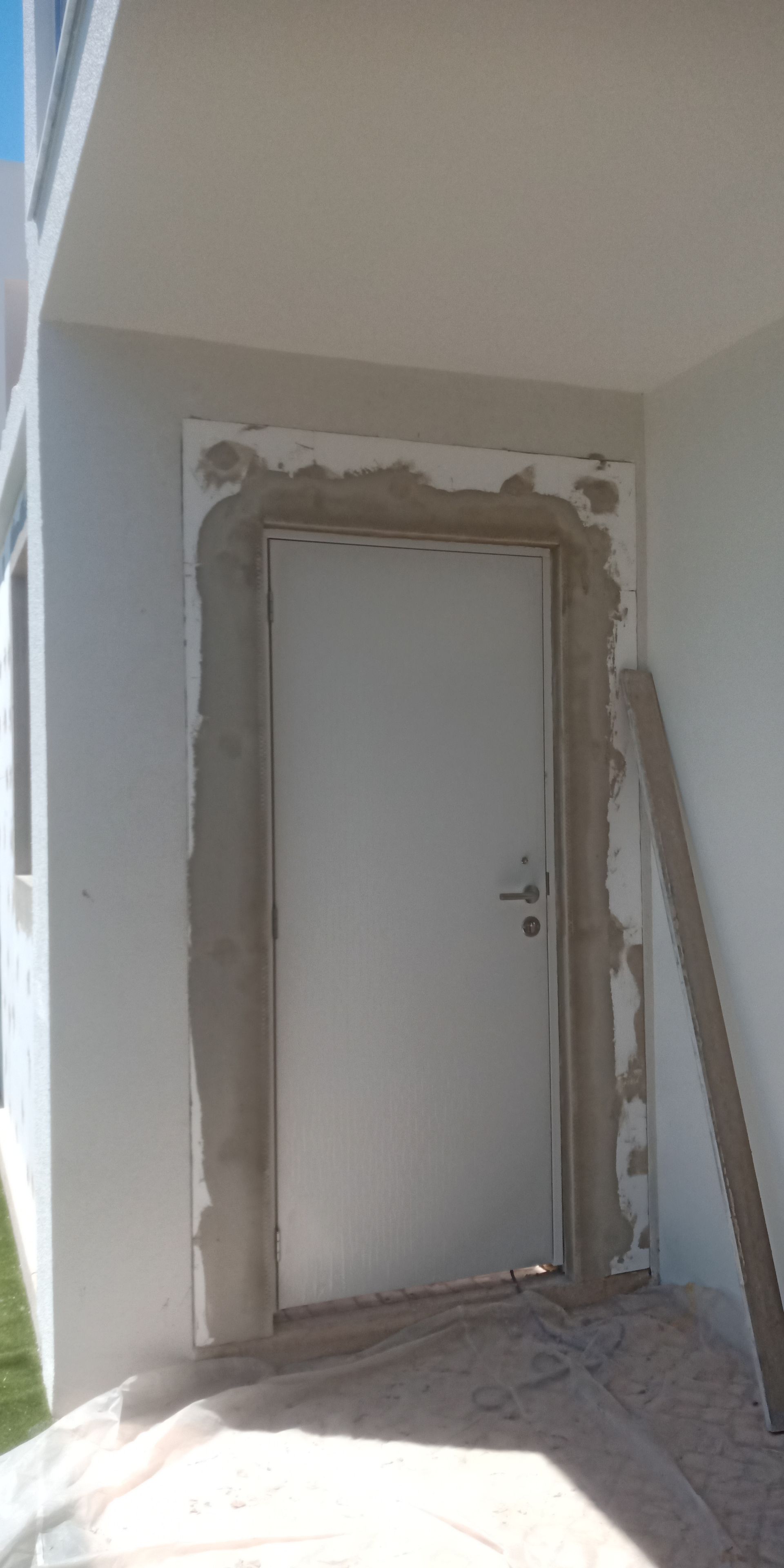 Porta branca com moldura de concreto inacabado em uma parede externa.